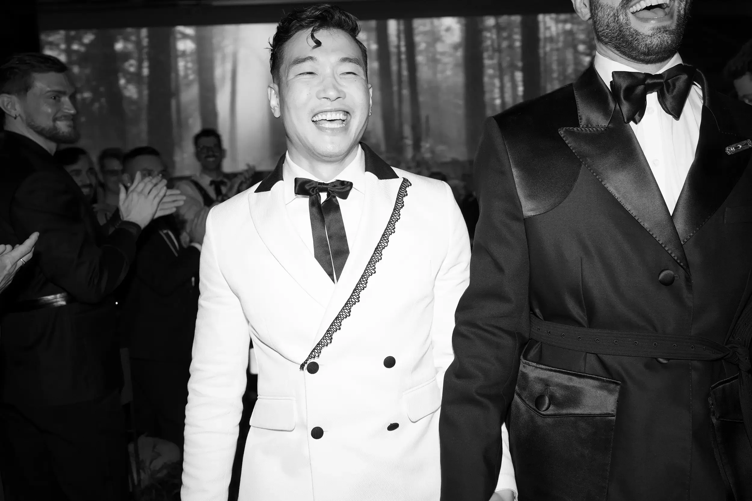 Two grooms during their recessional with their friends and family smiling and clapping.