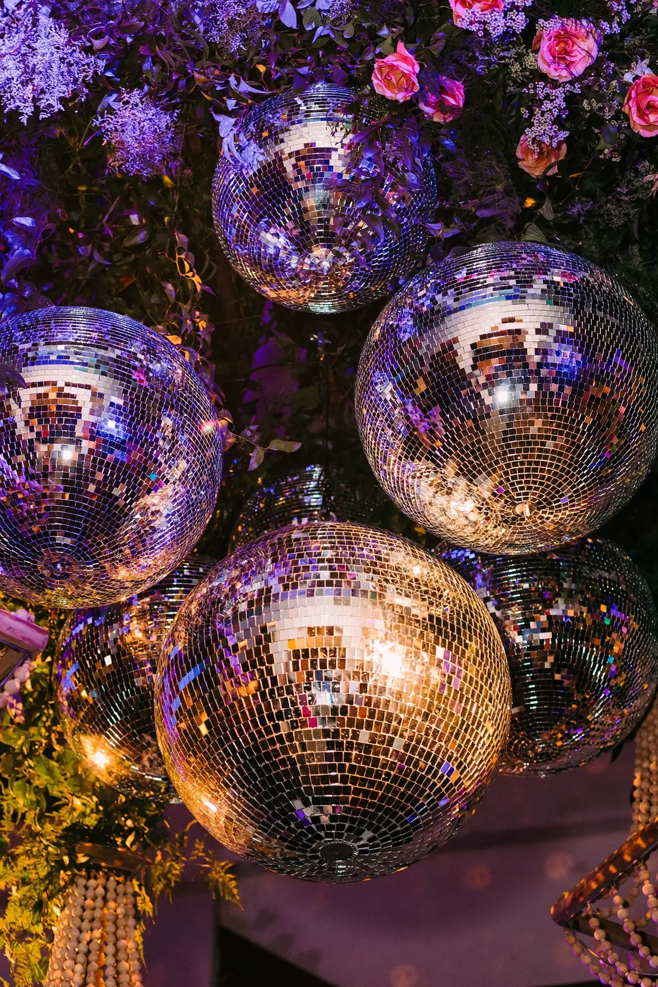Multiple disco balls hanging among purple and pink flowers and greenery.