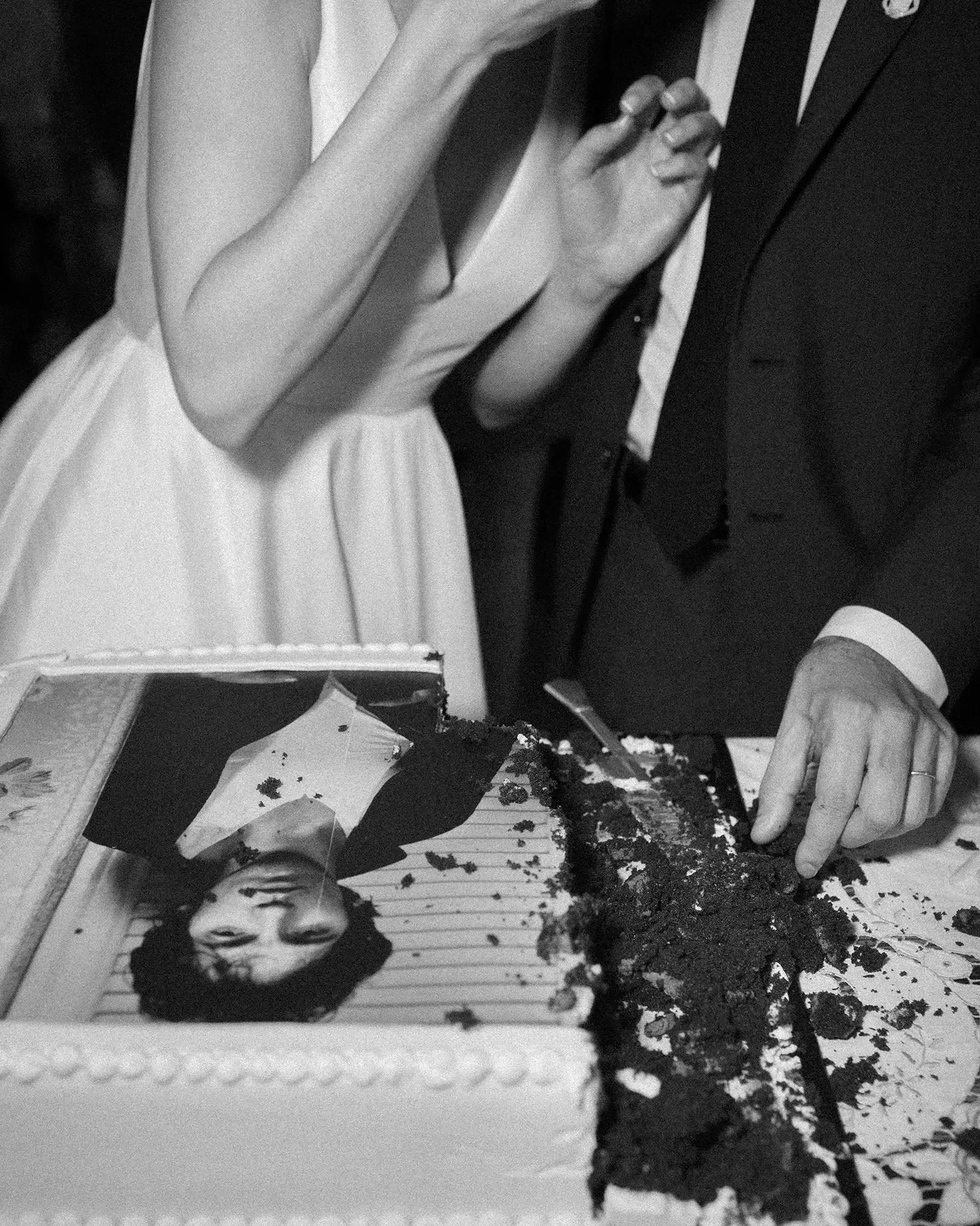 A black-and-white photo showing a woman in a white dress and a man in a tuxedo cutting a wedding cake decorated with a photograph of a bruce springsteen
