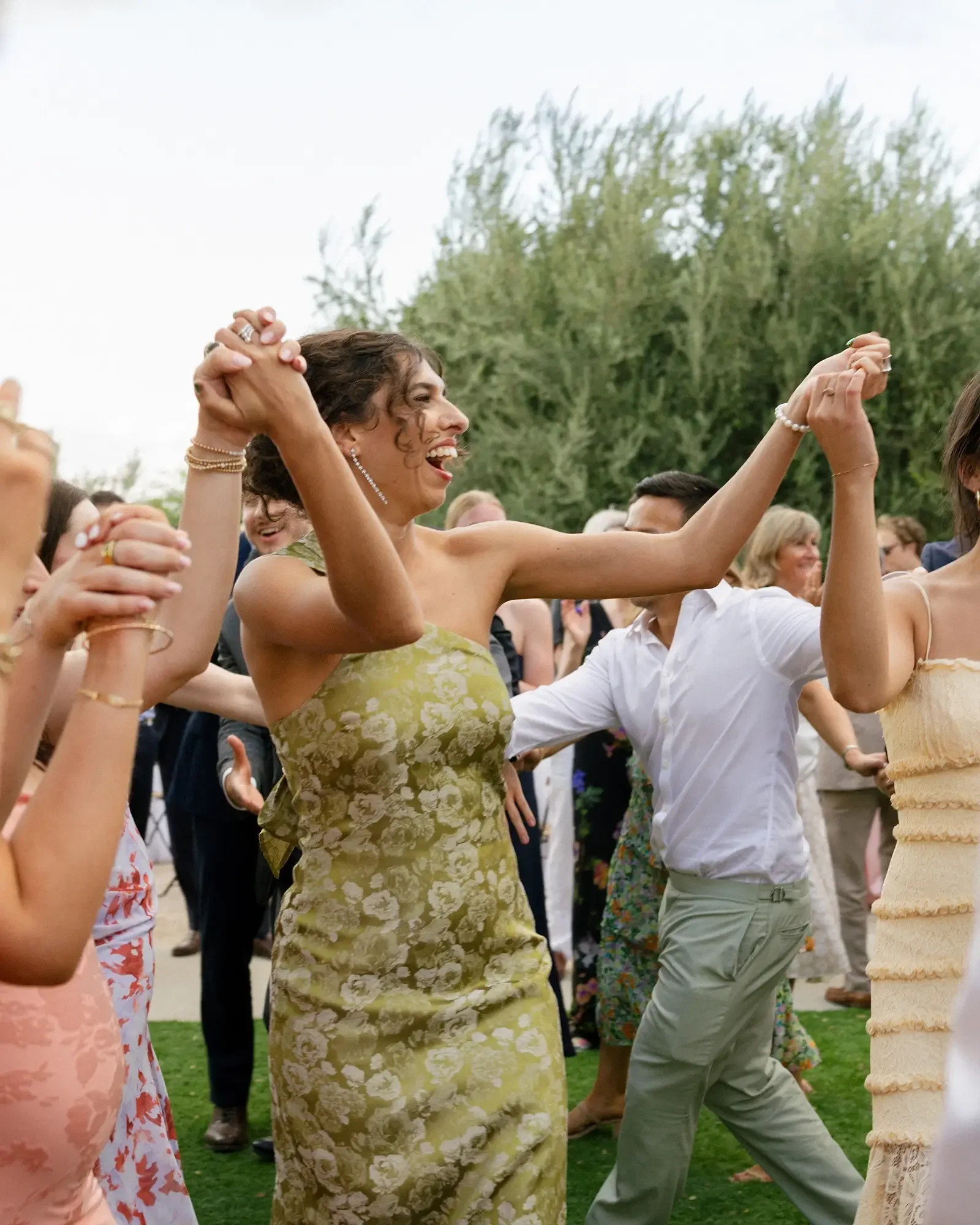 Wedding guests dancing outdoors at a wedding, holding hands and smiling.