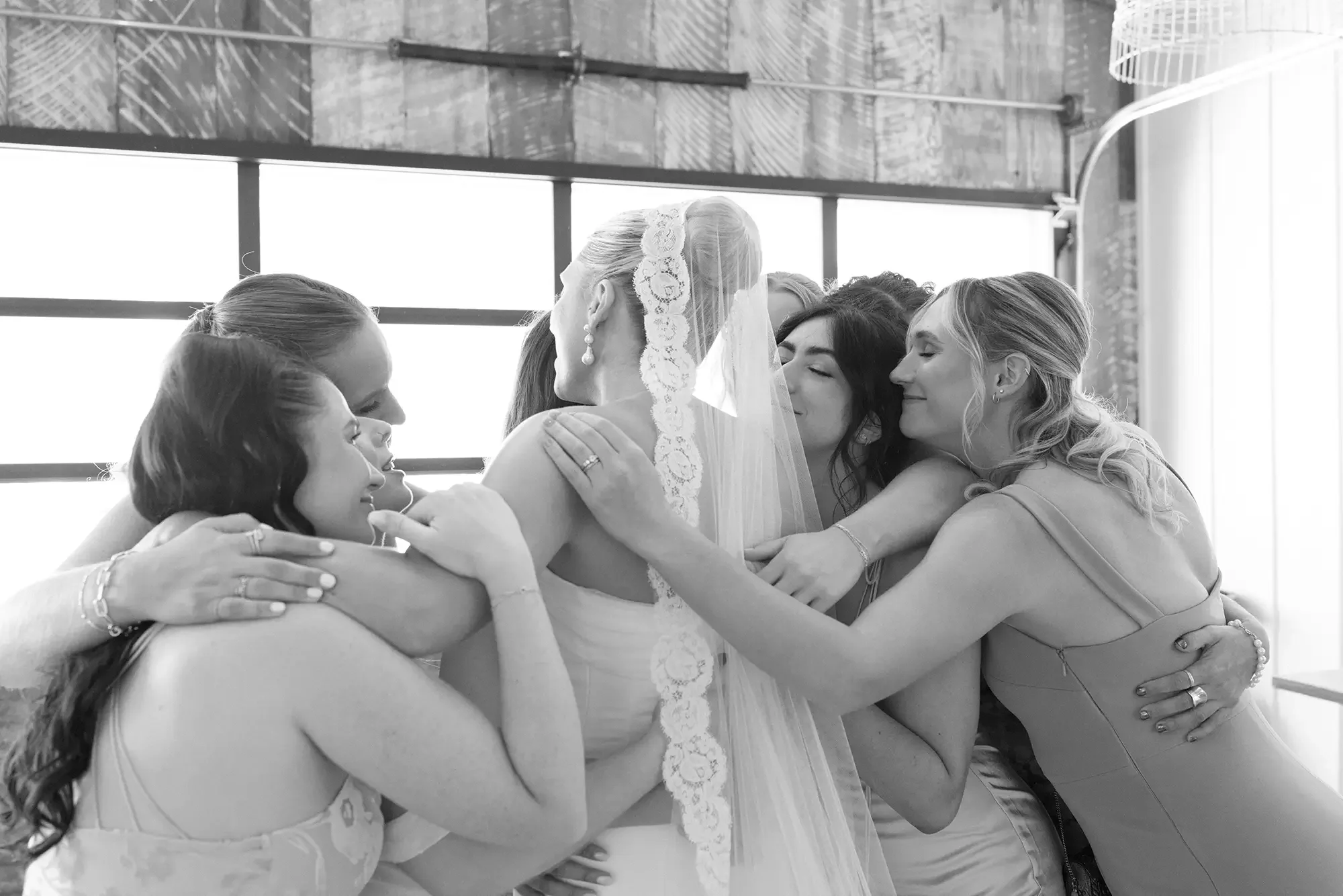 A bride in wedding dress and veil hugging and being embraced by the women in her wedding party