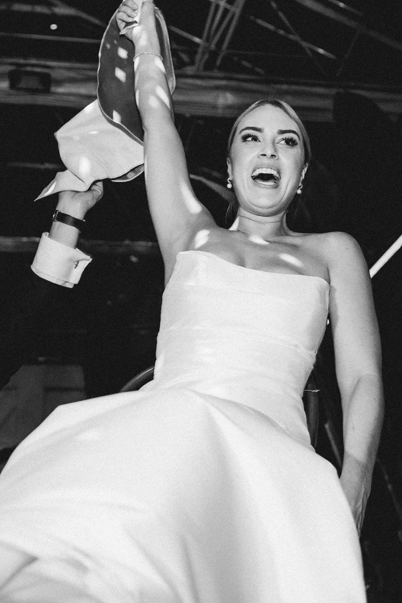A bride in a strapless white dress, smiling and raising her arm, during the hora at her wedding reception