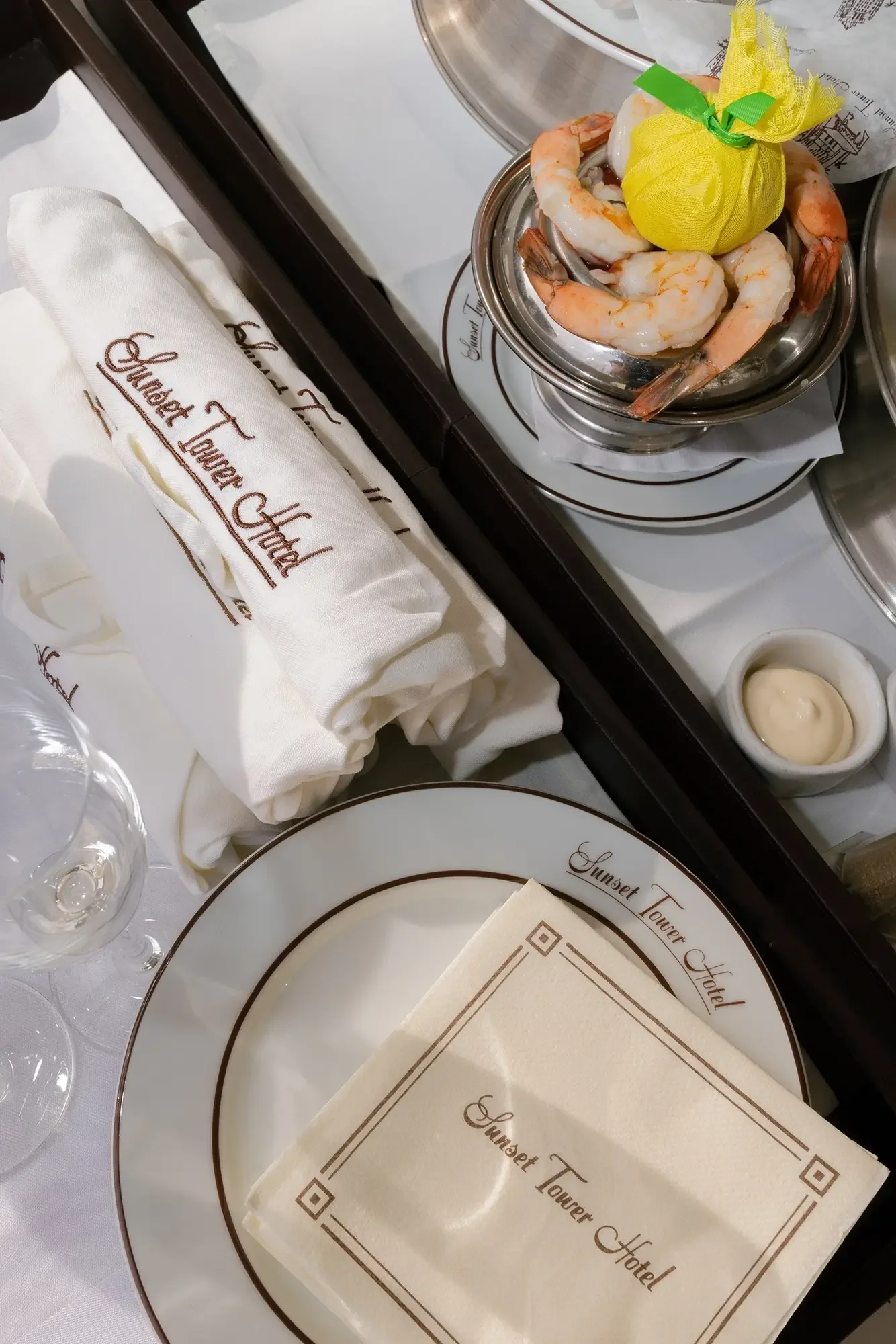 Shrimp cocktail served with a lemon wrapped in yellow netting on a small plate, with a small dish of cocktail sauce, set on a table at Sunset Tower Hotel.