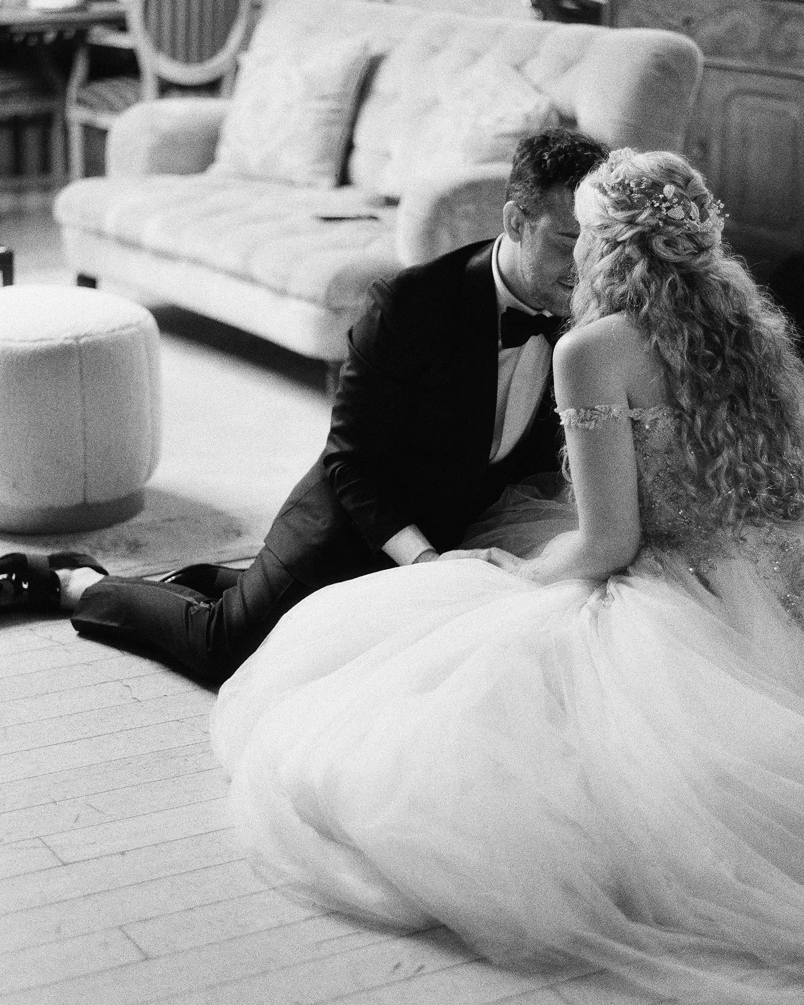A bride and groom share a kiss on the floor of the bridal suite during their wedding, with the bride in a wedding dress and the groom in a tuxedo.