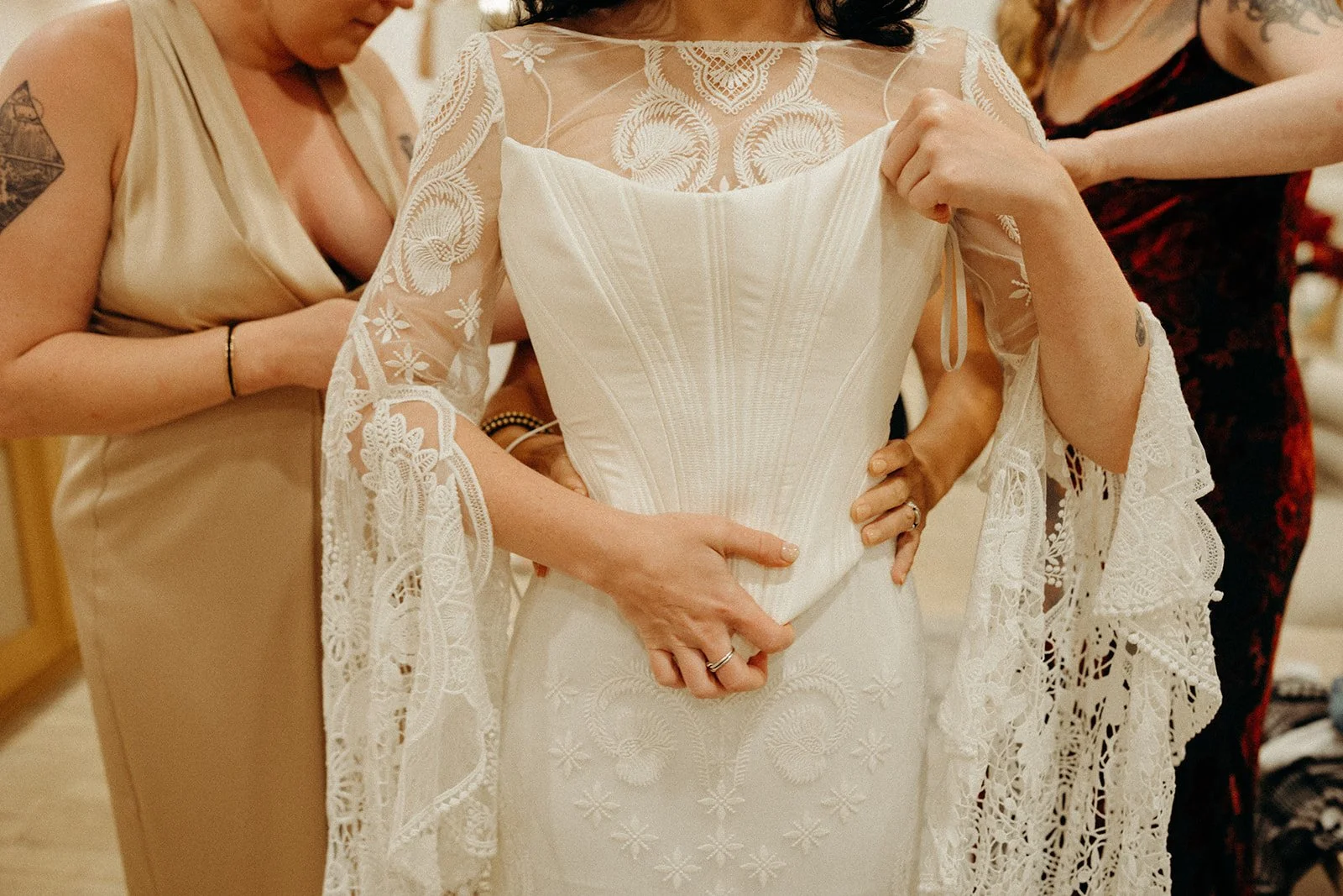 A woman in a white wedding dress being assisted by others before a wedding.
