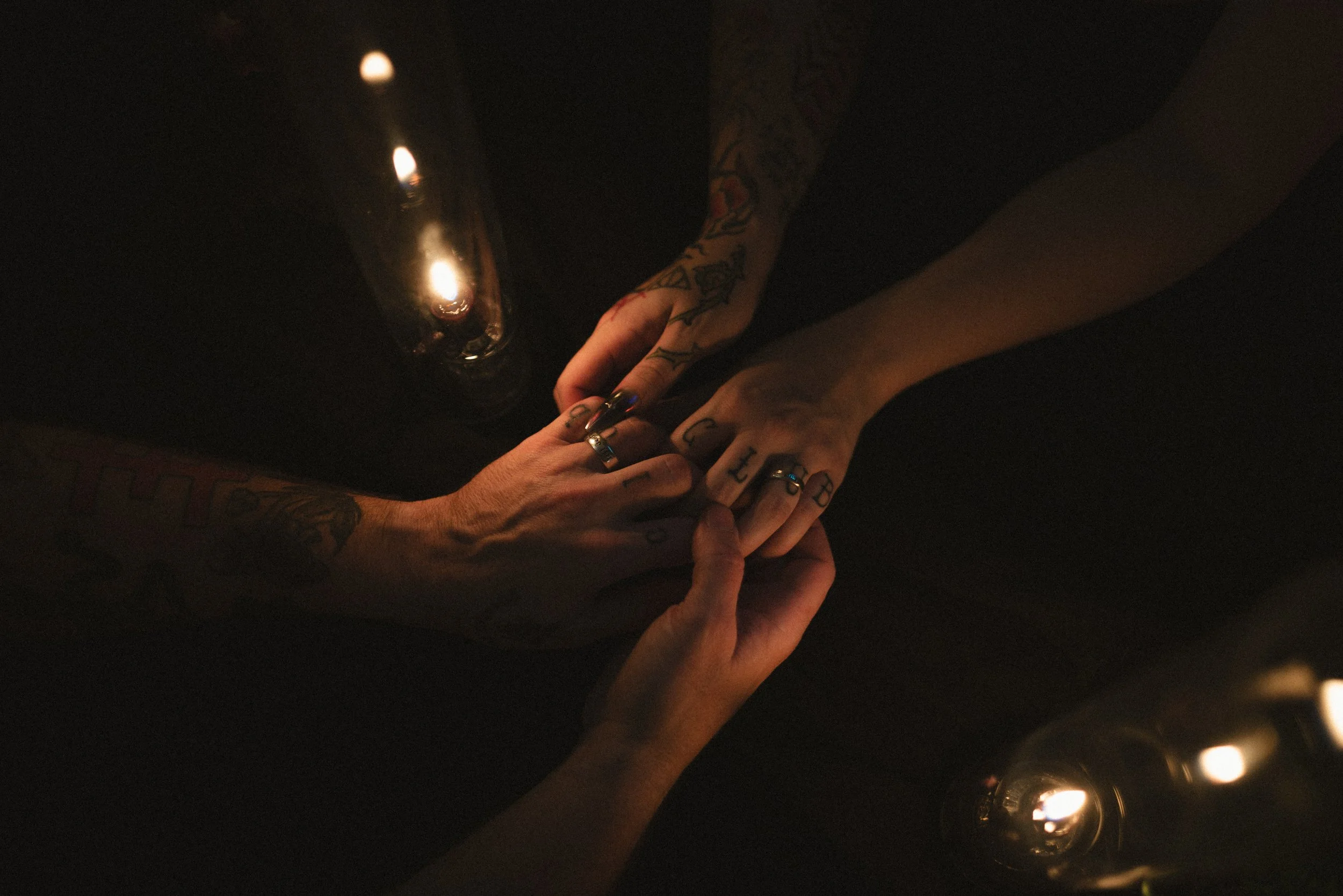 Tattooed hands with rings clasped together in warm candlelight