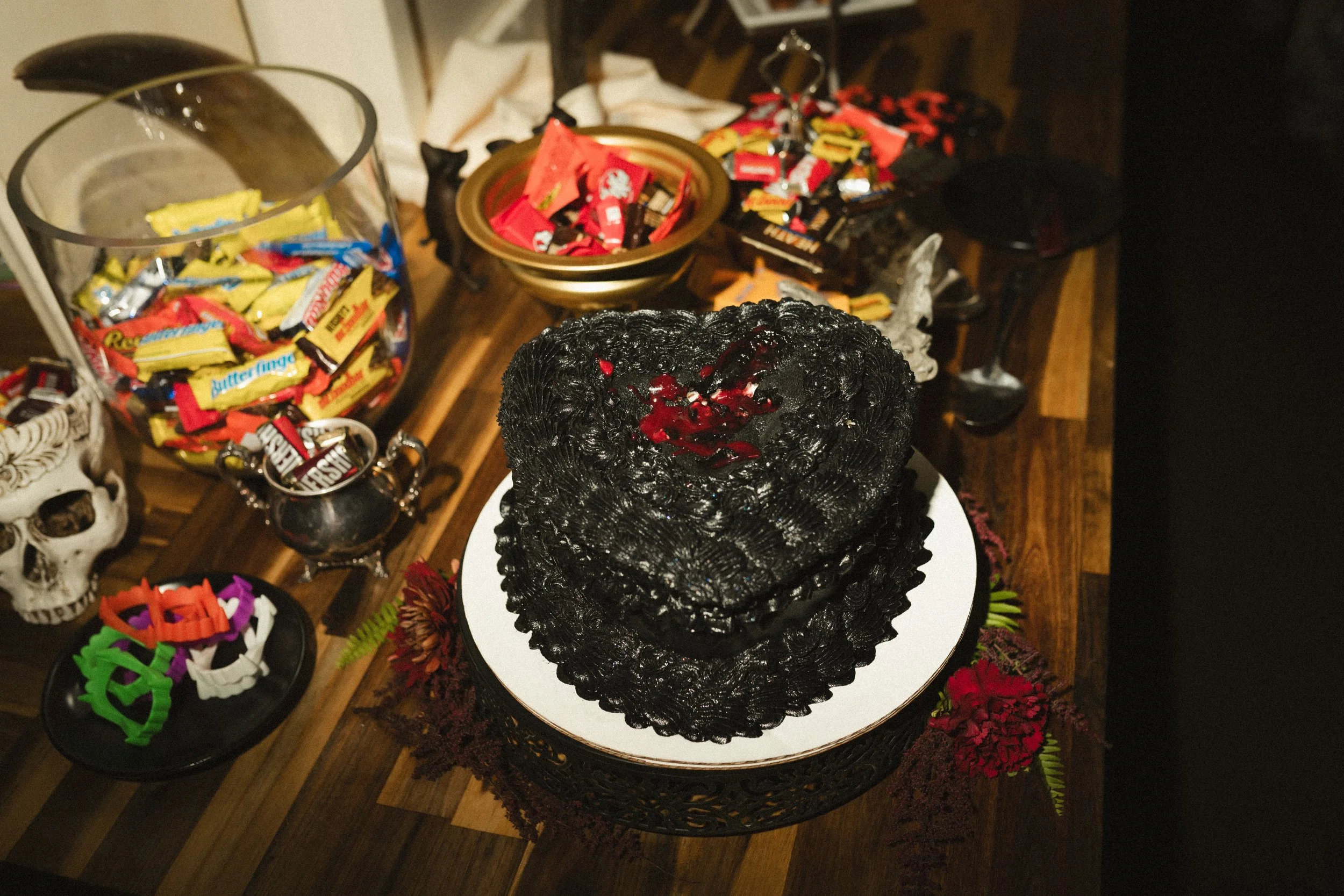 Black Halloween cake with red filling on a white plate, surrounded by candy and spooky decorations.
