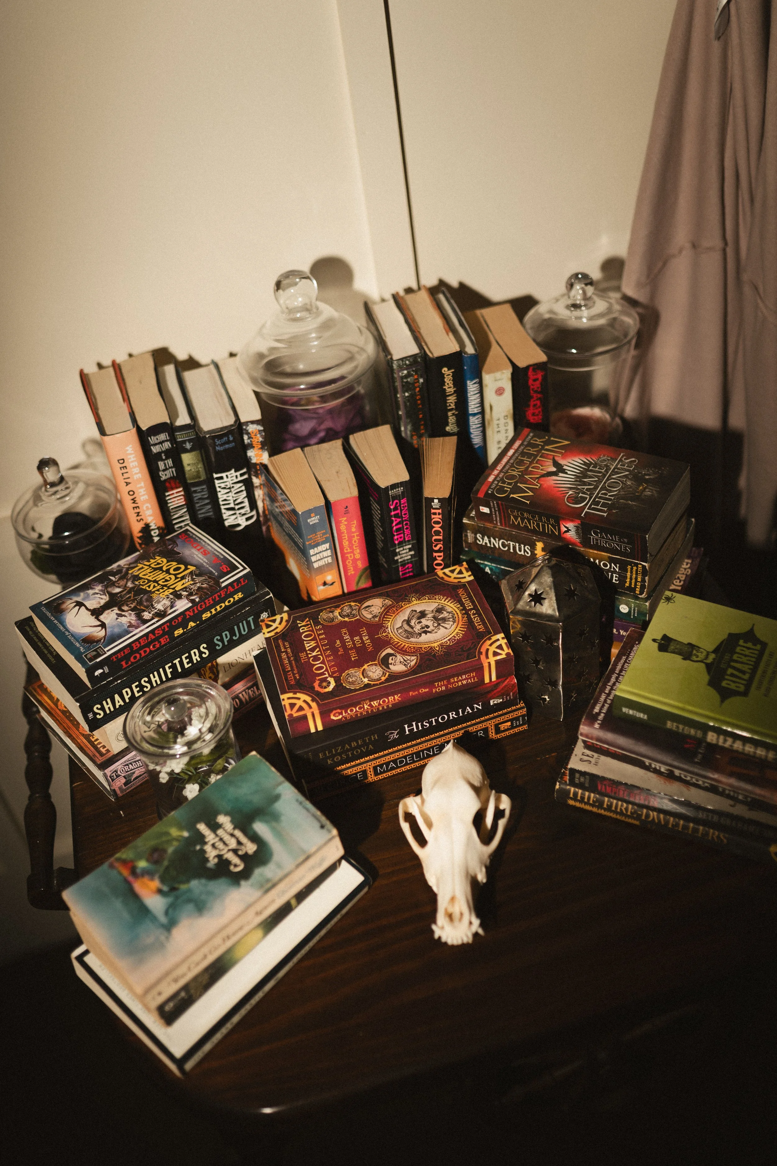 Vintage books piled on a dark wooden table with glass candle holders and a small skull ornament.