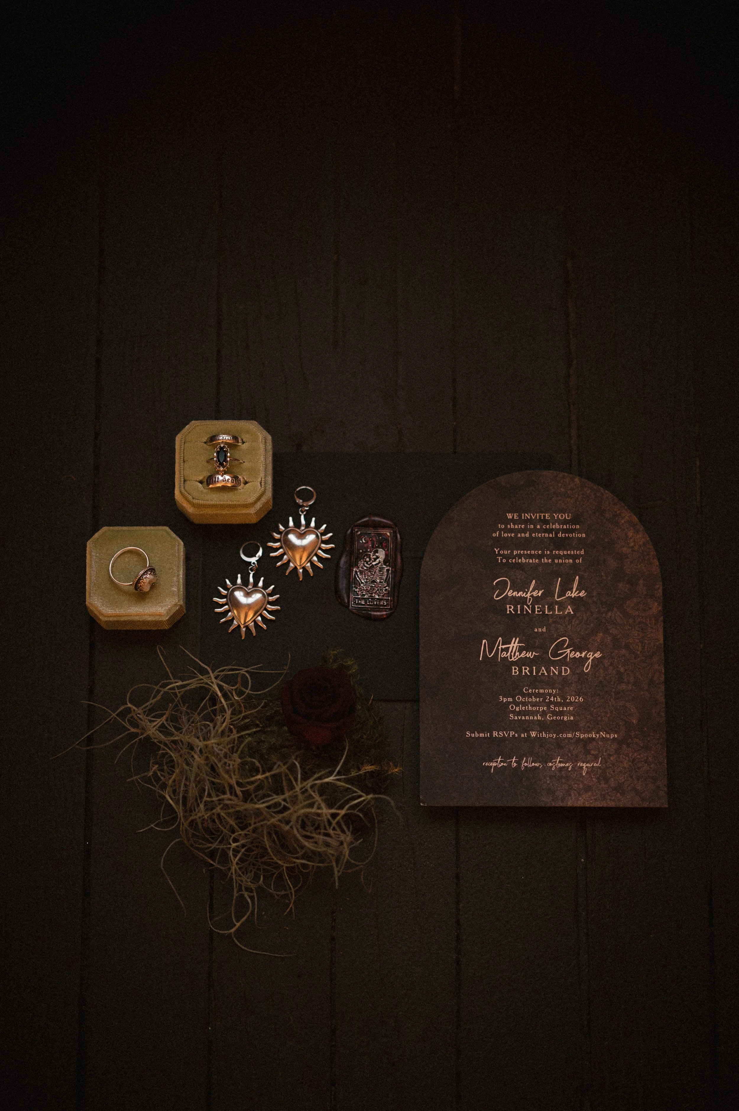 Dark gothic wedding flat lay featuring antique jewelry, heart-shaped pendants, tarot cards, dried flowers, and a rustic wedding invitation.