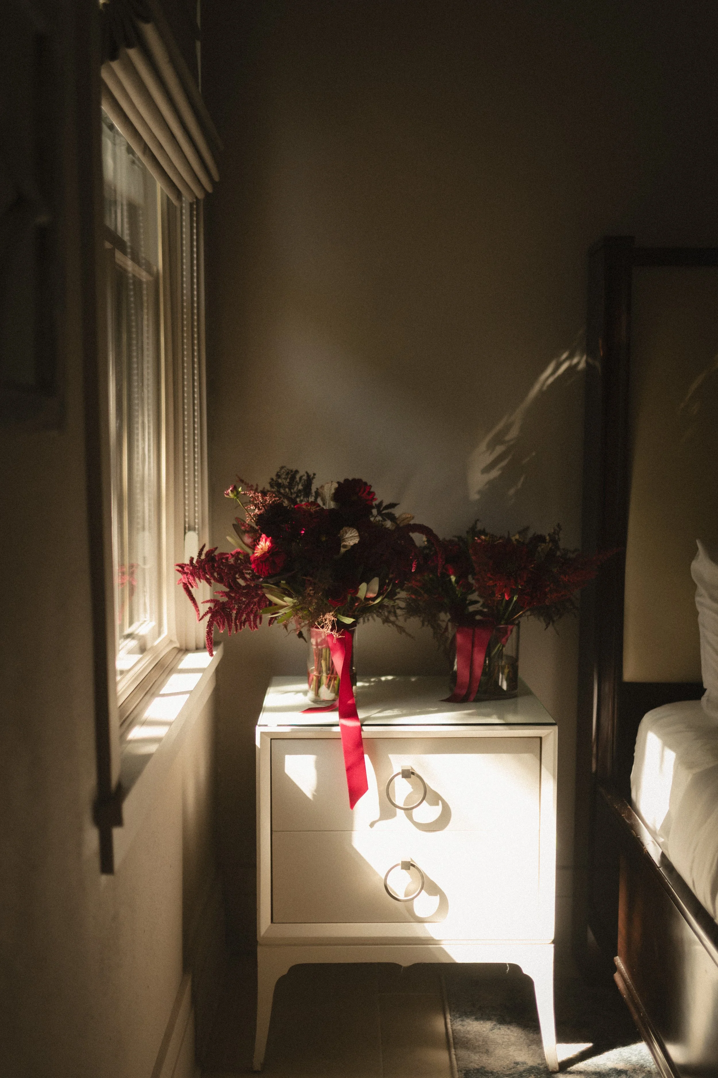 Sunlit room with red flower bouquets in glass vases on a white cabinet beside a window