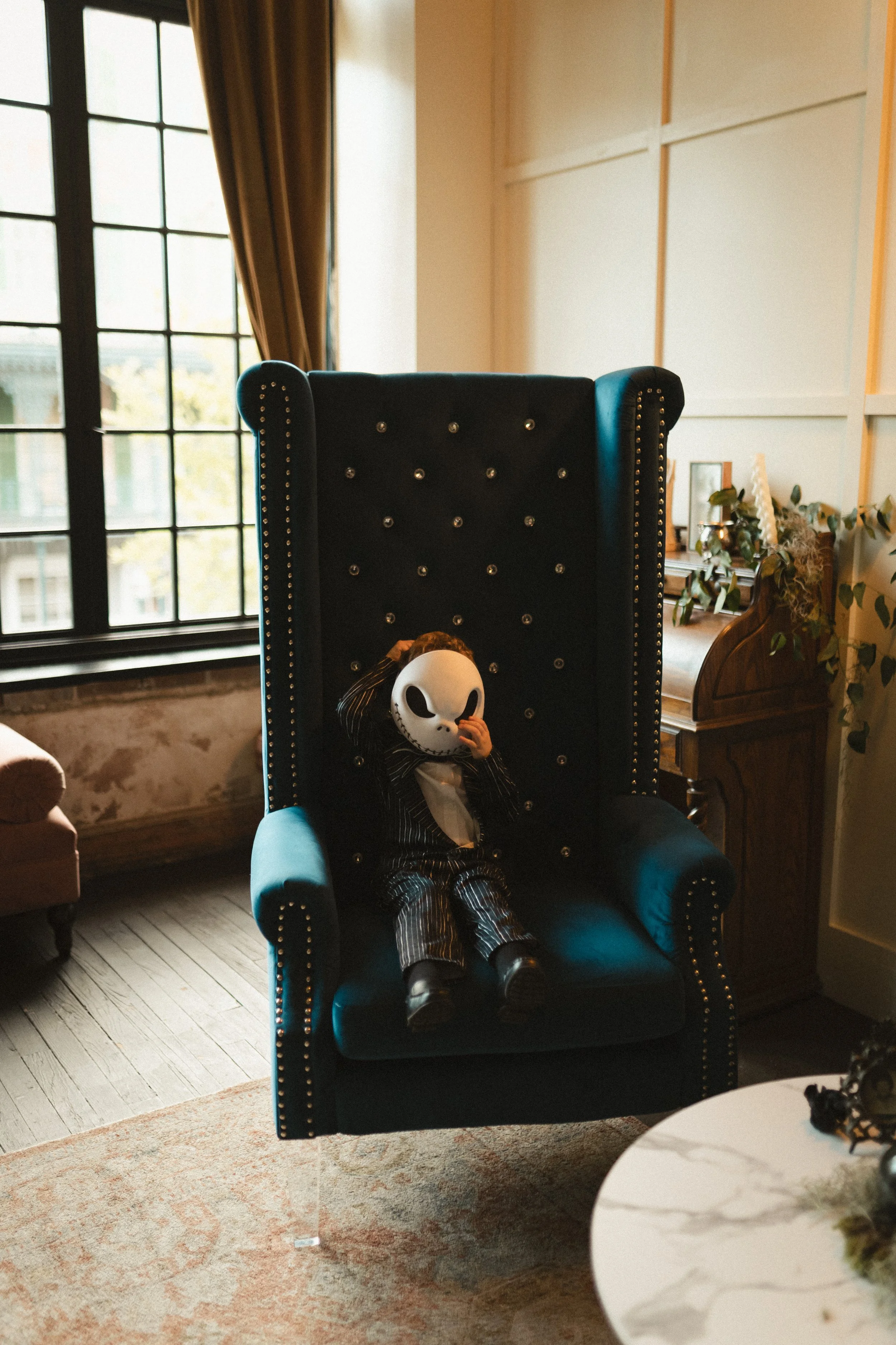 Child dressed as Jack Skellington sitting in a black and teal wingback chair in a cozy living room