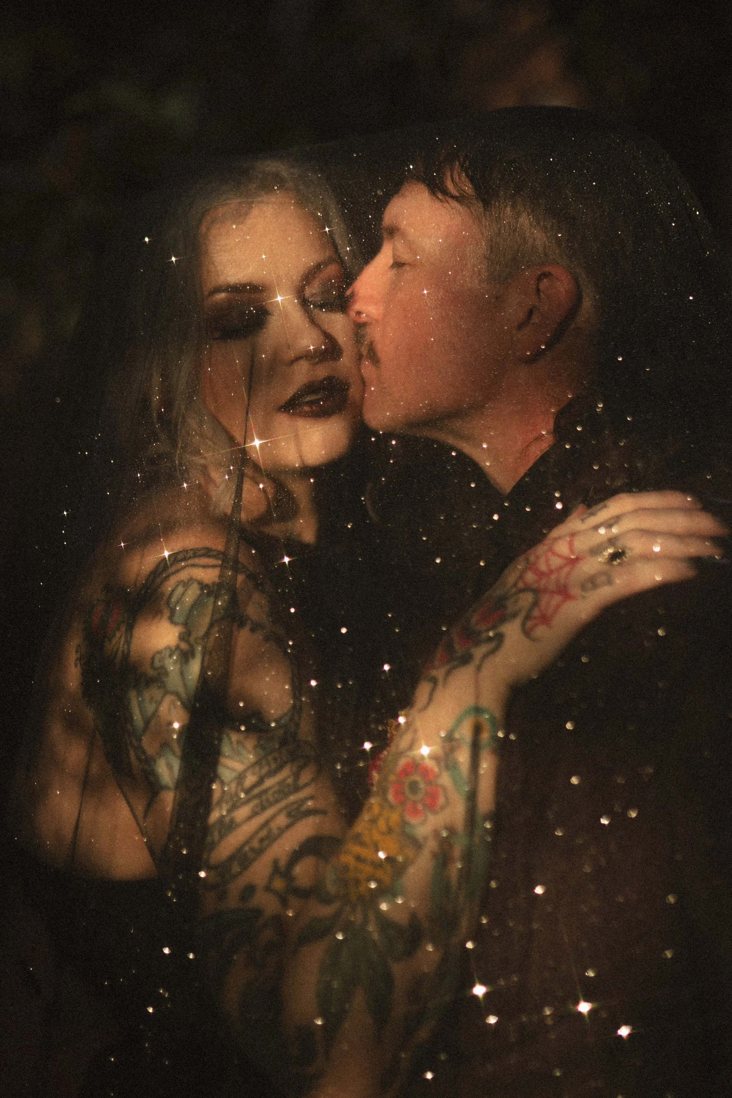 Tattooed couple kissing in a dimly lit setting with a sparkling star-filter effect