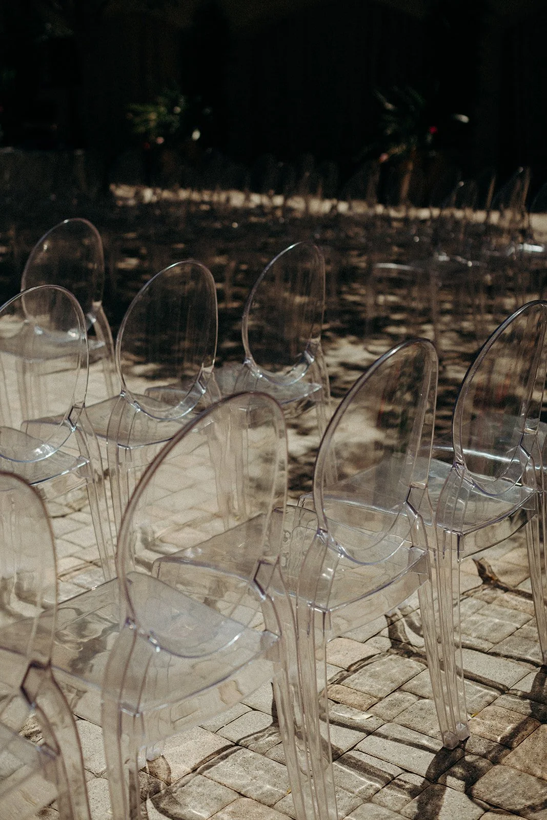 Row of clear plastic chairs on paved outdoor surface at evening time.