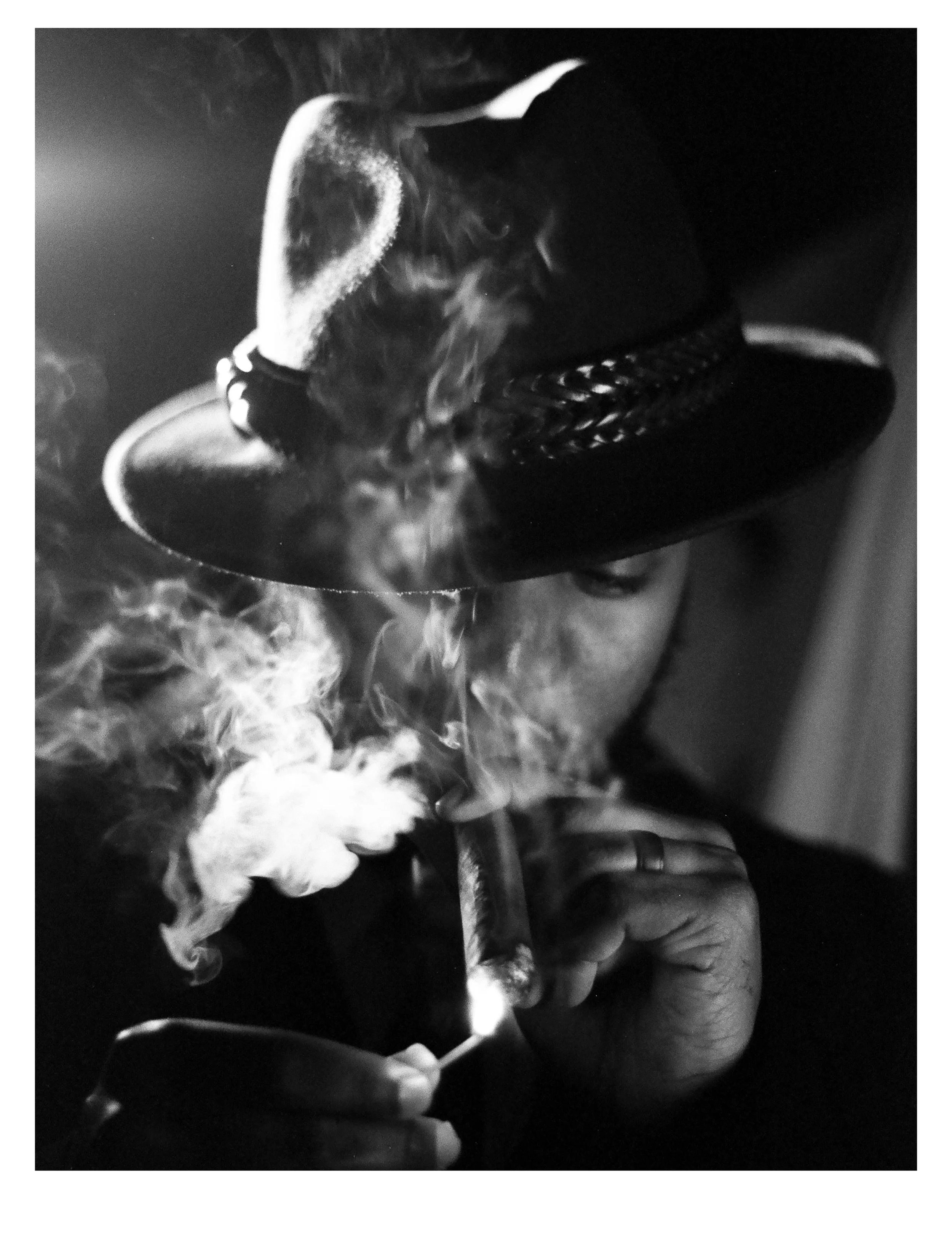 A person wearing a hat with a chain, smoking a cigarette, with smoke swirling around.