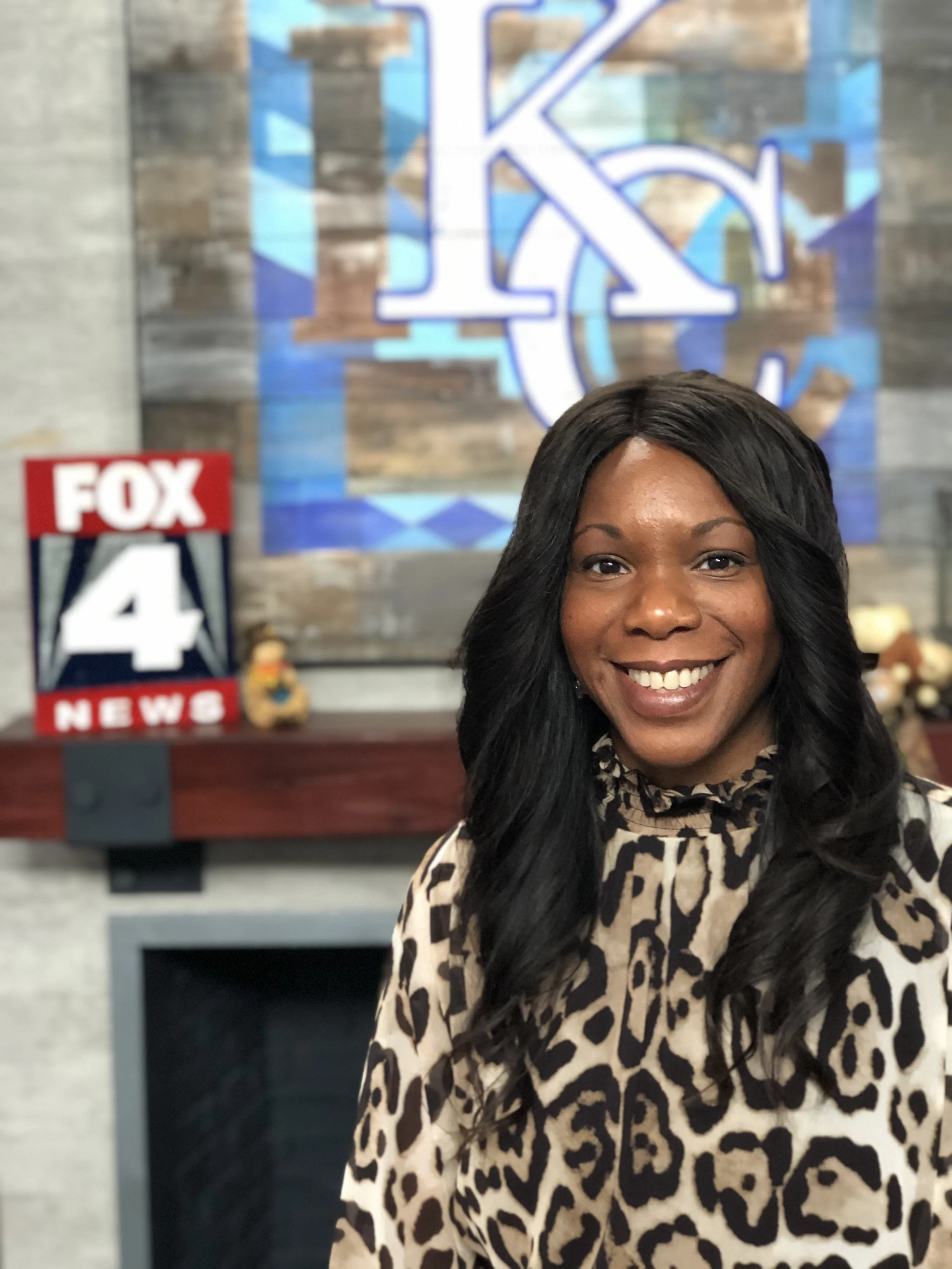 Person smiling in front of a Fox 4 News sign and a large KC logo.