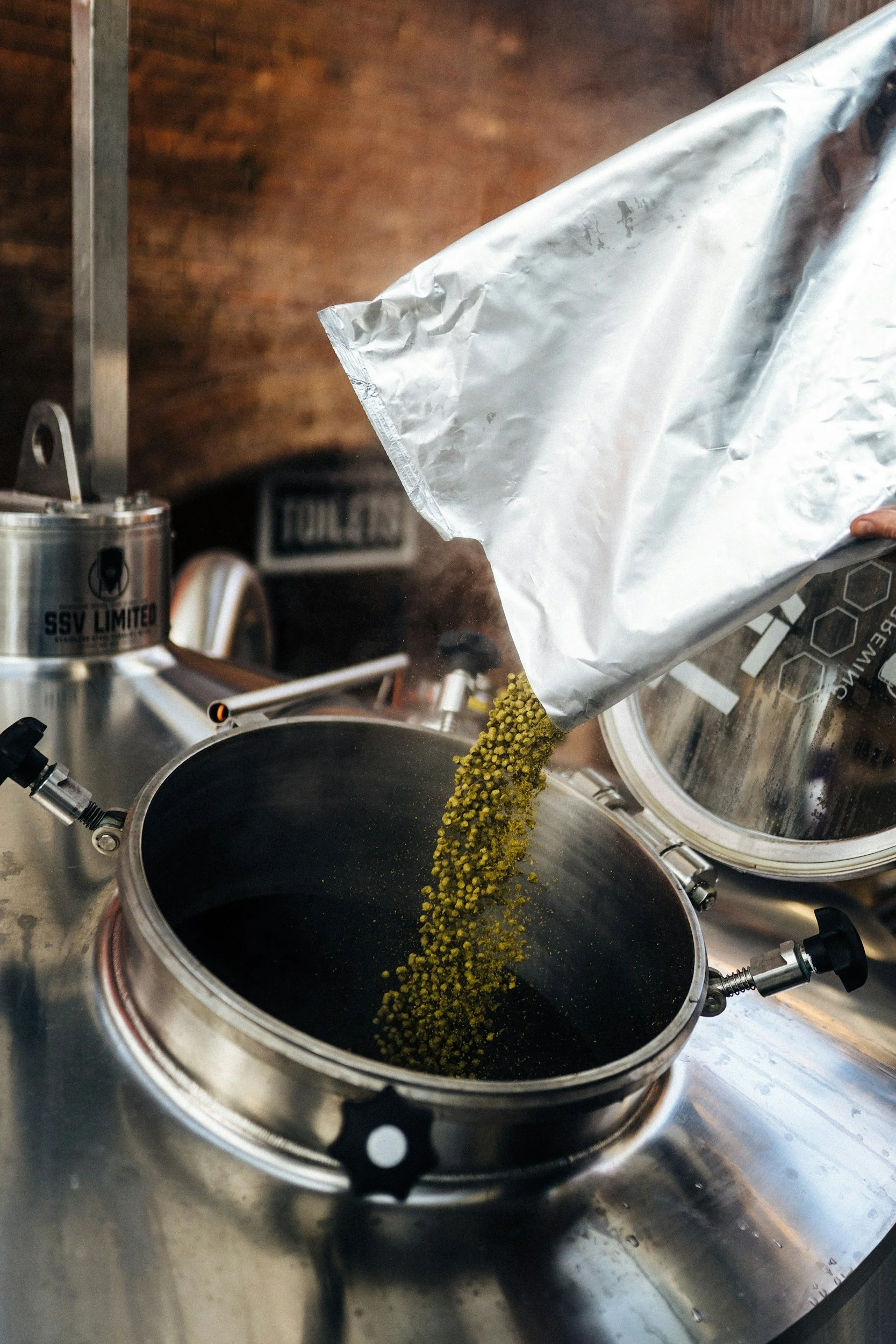 A person pouring yellowish-green grains into a black pot on a stove in a kitchen.