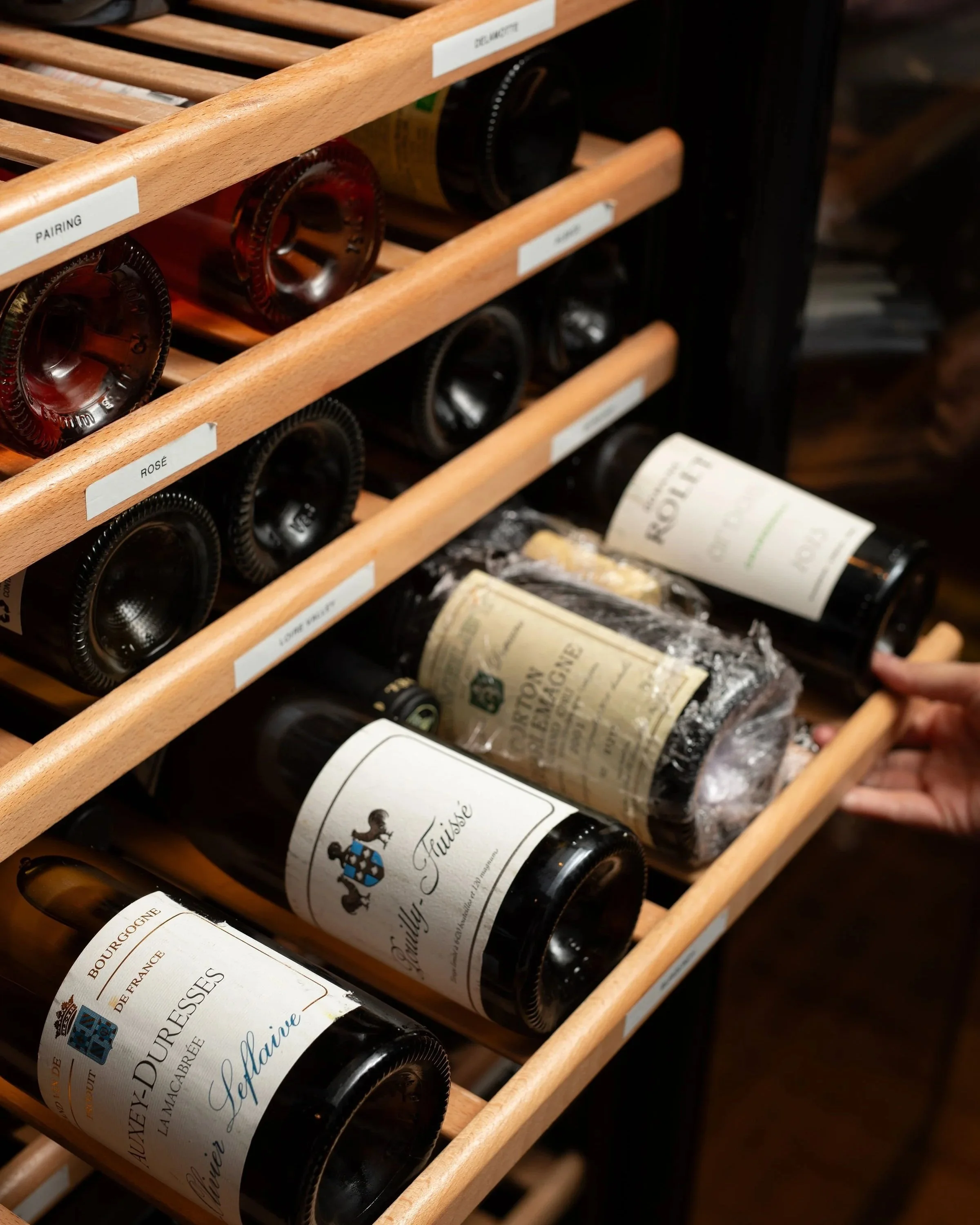 Bottles of wine stored horizontally in wooden wine racks, with labels for pairing and rosé wines.