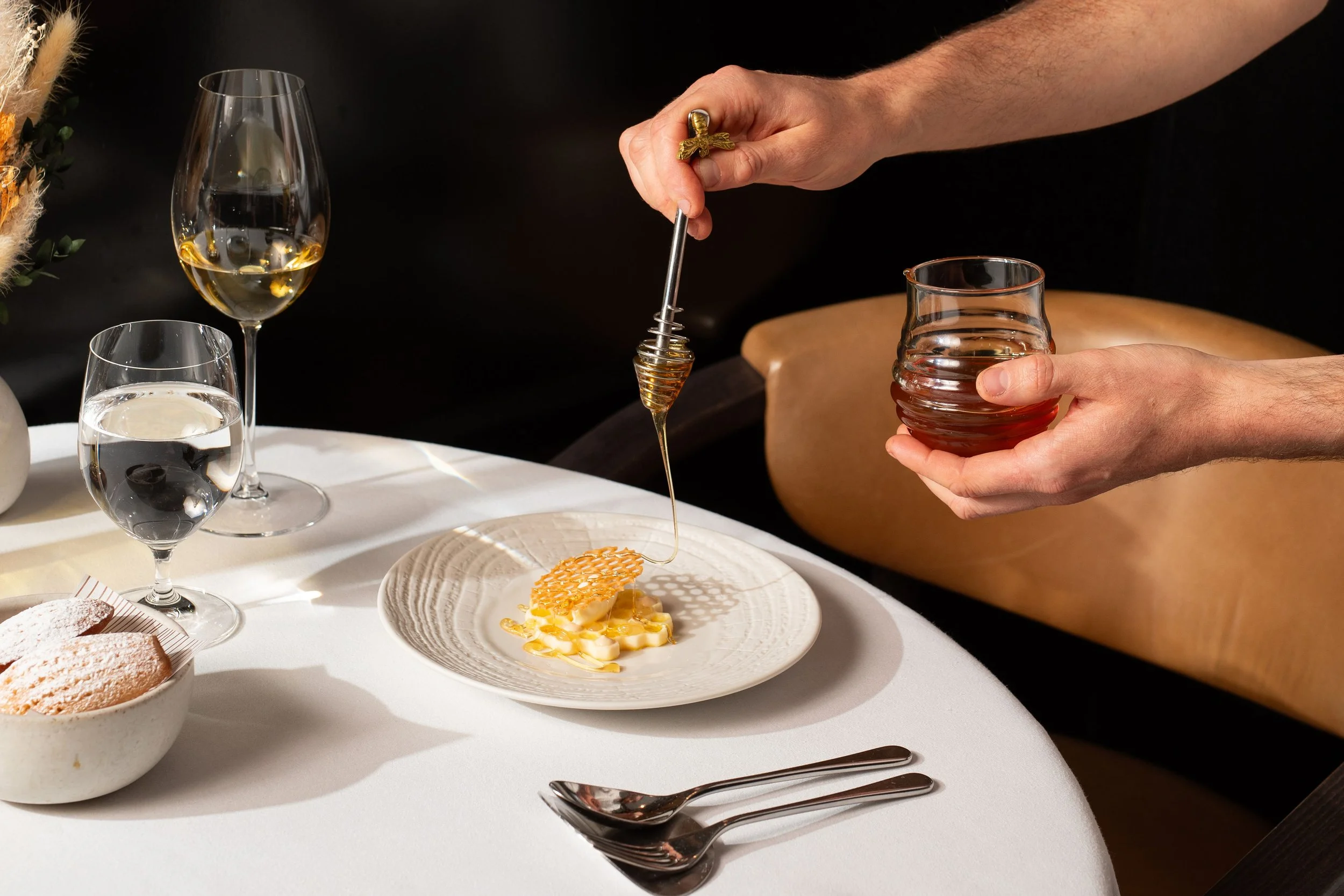 Chef drizzling honey over a plated dessert with a honeycomb garnish at an elegant restaurant table