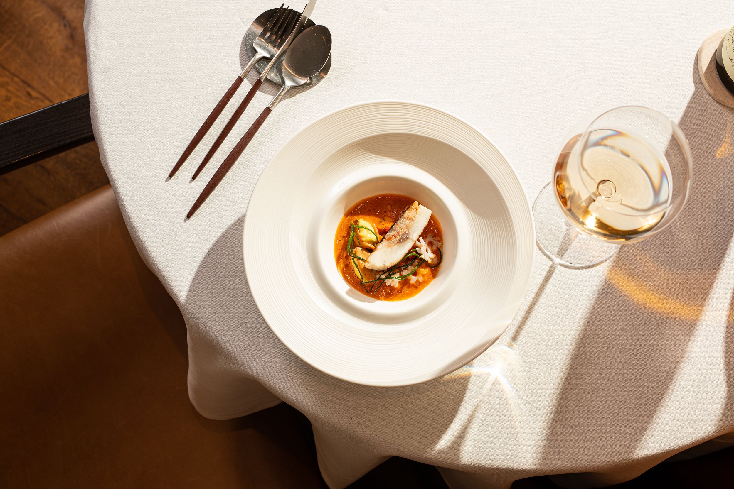 Elegant restaurant table with plated fish in sauce, silverware, and a glass of white wine