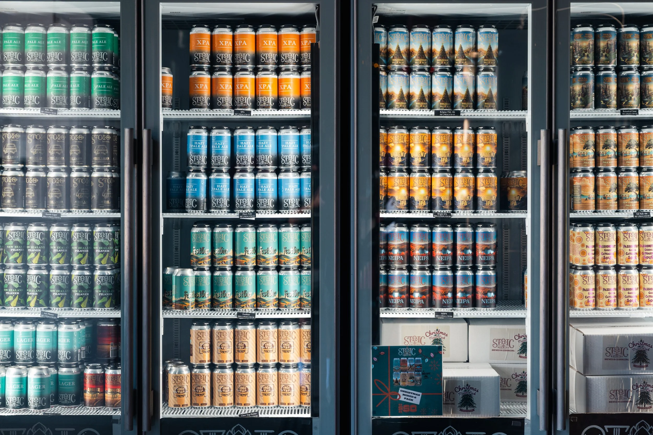 Display of various craft beers in cans inside a refrigerated store shelf, with different colorful labels and packaging.