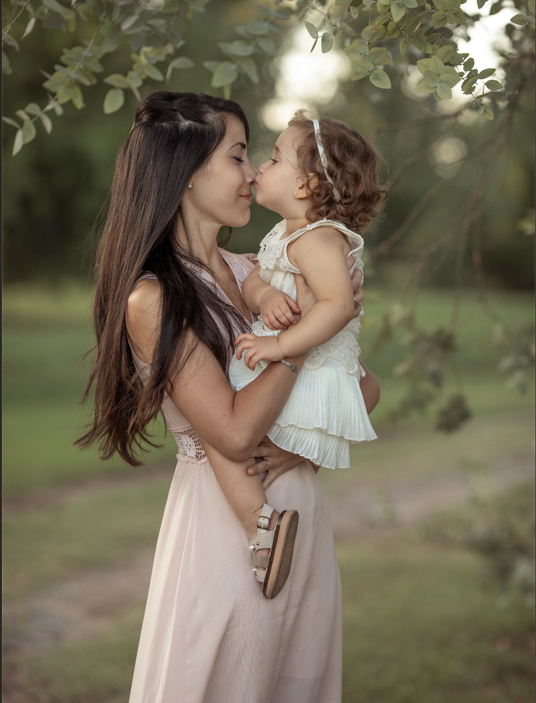 Mujer y niña en un entorno natural, tocándose la nariz y casi tocándose sus frentes, expresión de cariño y ternura.