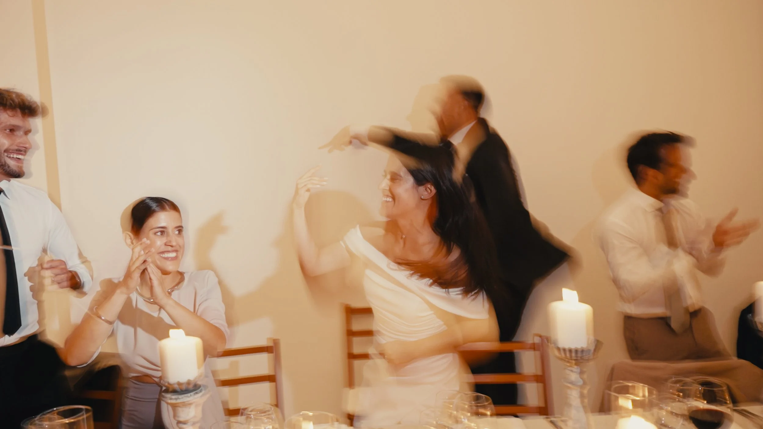 People celebrating at a dinner party with candles, smiling and interacting in a lively atmosphere.