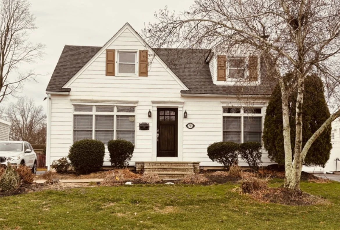 Before exterior of Cape Cod home in New York with outdated siding and landscaping.