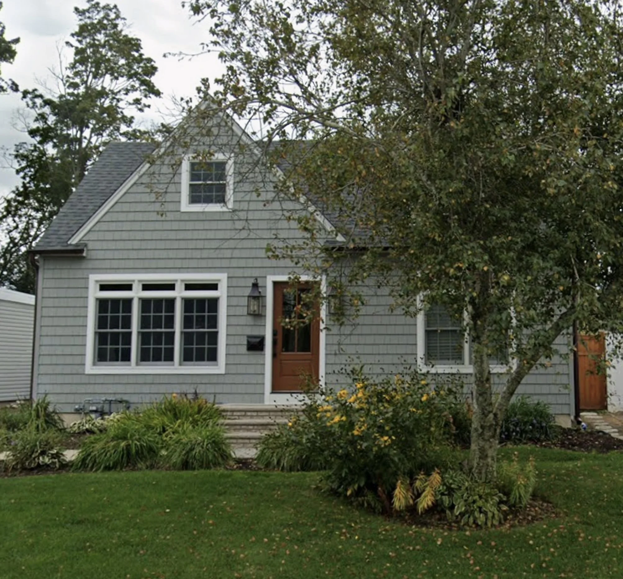 Updated Cape Cod home exterior in New York with green siding, white trim, and improved landscaping.