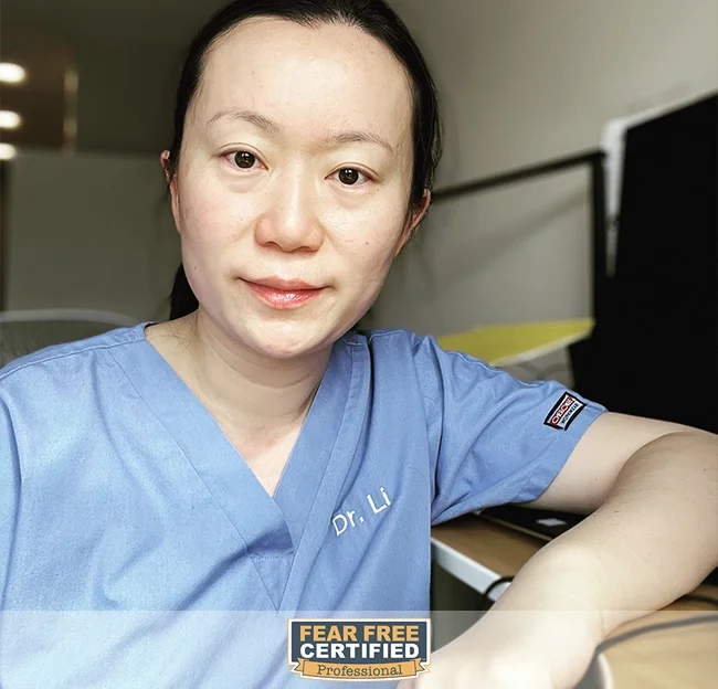 A woman in blue scrubs with 'Dr. Li' embroidered on it, sitting at a desk, smiling slightly, with a 'Fear Free Certified Professional' badge at the bottom of the image.
