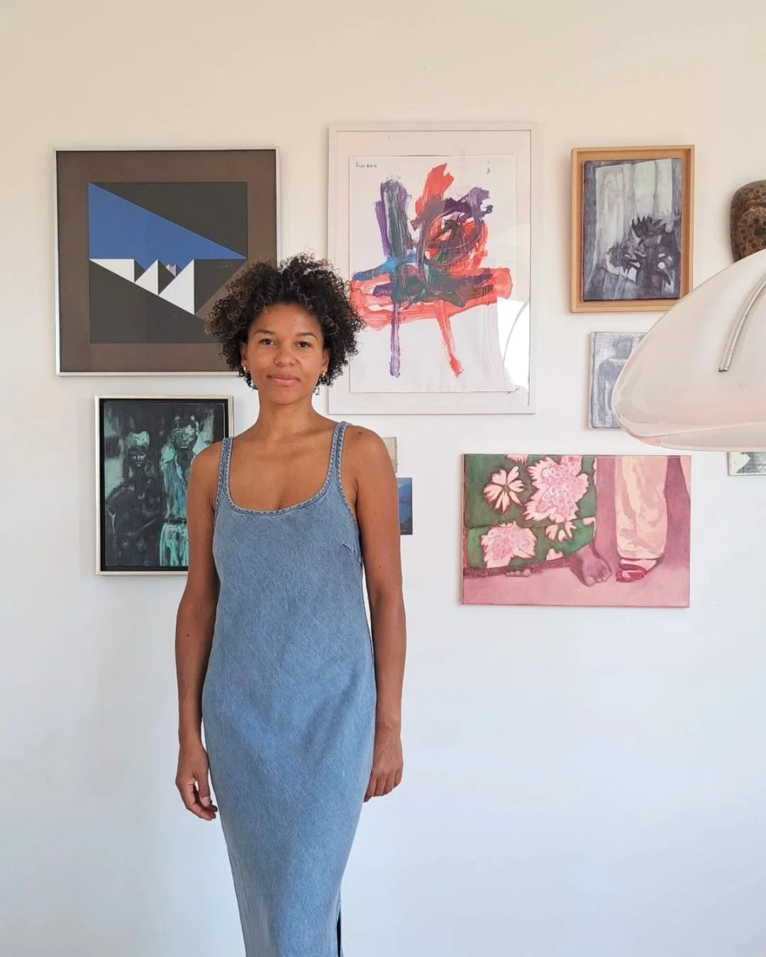 A woman in a blue dress standing in front of an art gallery wall with various abstract and figurative paintings.