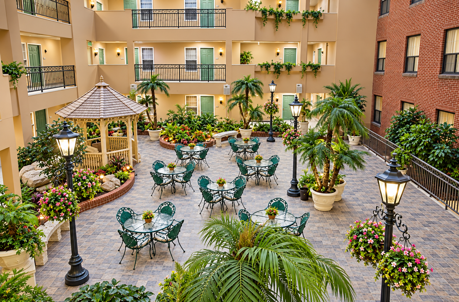 Indoor courtyard with outdoor tables and chairs, potted plants, palm trees, flower beds, a decorative gazebo, and vintage-style street lamps.