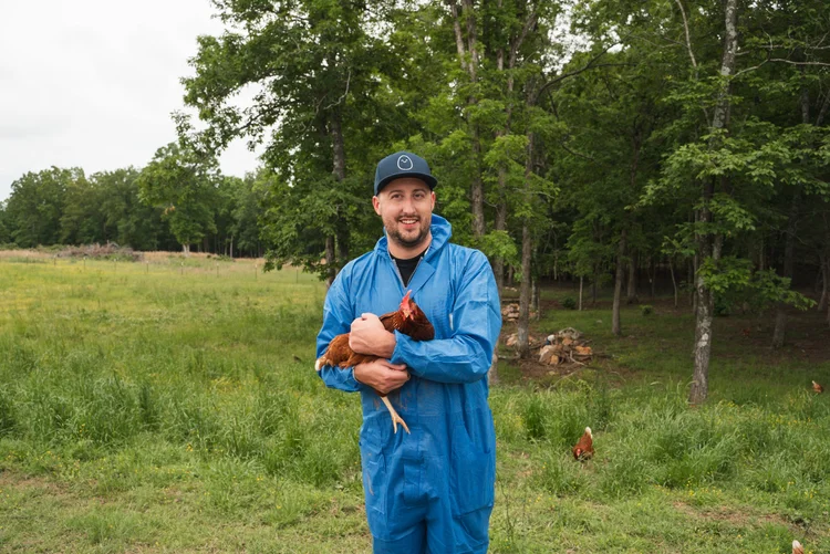 Ryan Peters of Peters Pasta holding a chicken on a farm during a YouTube video production with Orchard Eight Media