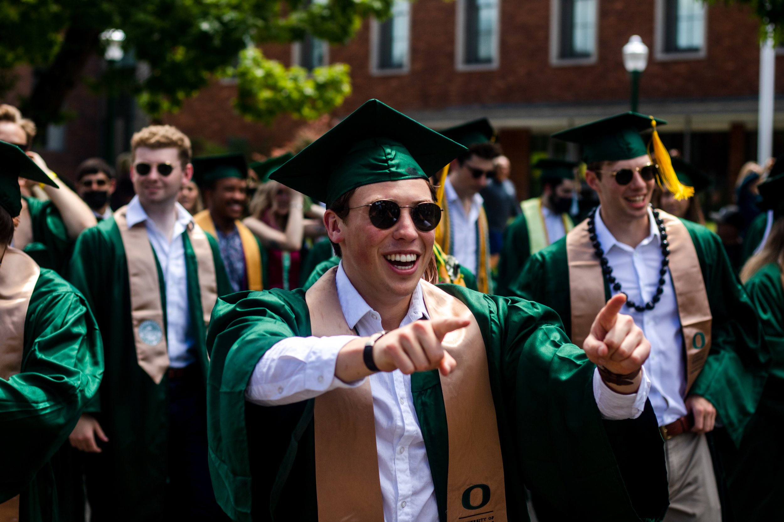 A University of Oregon graduate gestures towards someone in the crowd during the traditional Grad Parade. After a full academic year of online school, the class of 2021 participated in the University of Oregon's traditional Grad Parade on June 12, 2