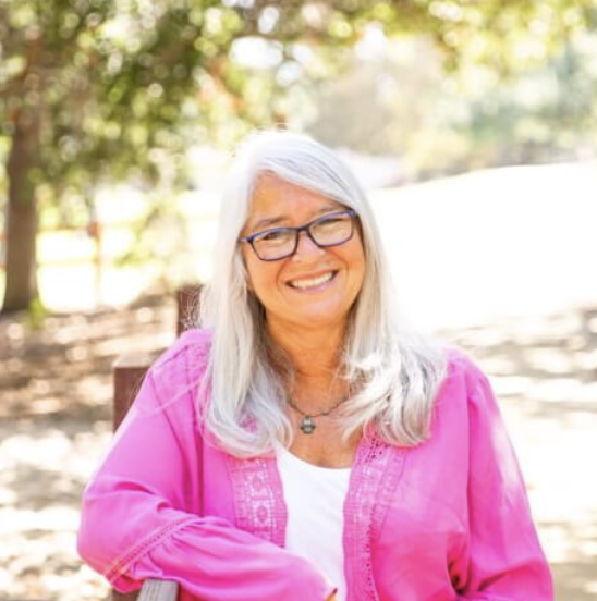 Trustee Cindy Goldberg wearing a pink jacket outdoors with trees in the background.