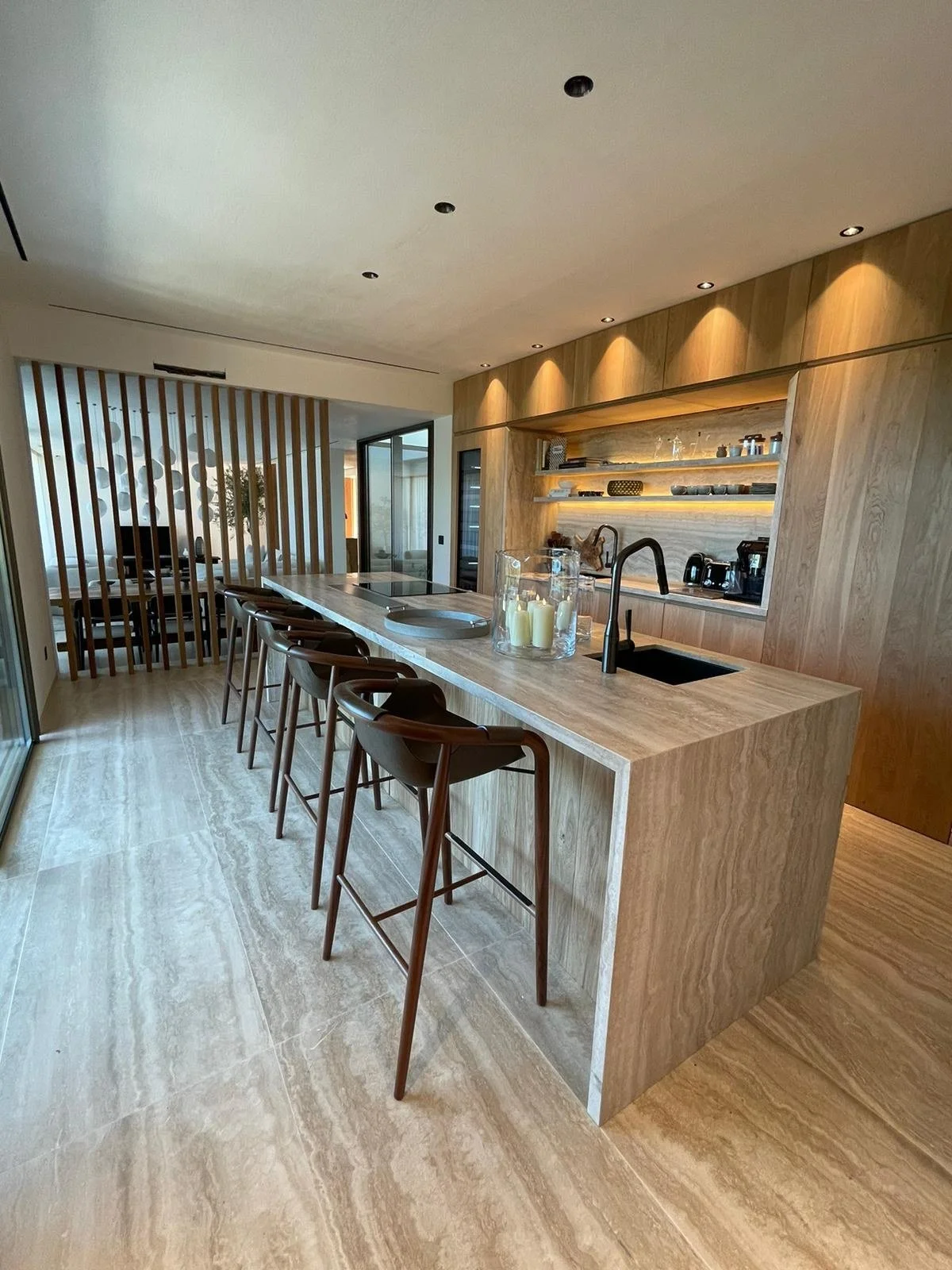 Kitchen — Completed build
Timber, stone and integrated light

The completed space retains the island arrangement, curved stools, recessed shelving and timber screen. Surface patterns, tap finishes and styling vary between the render and site photogra
