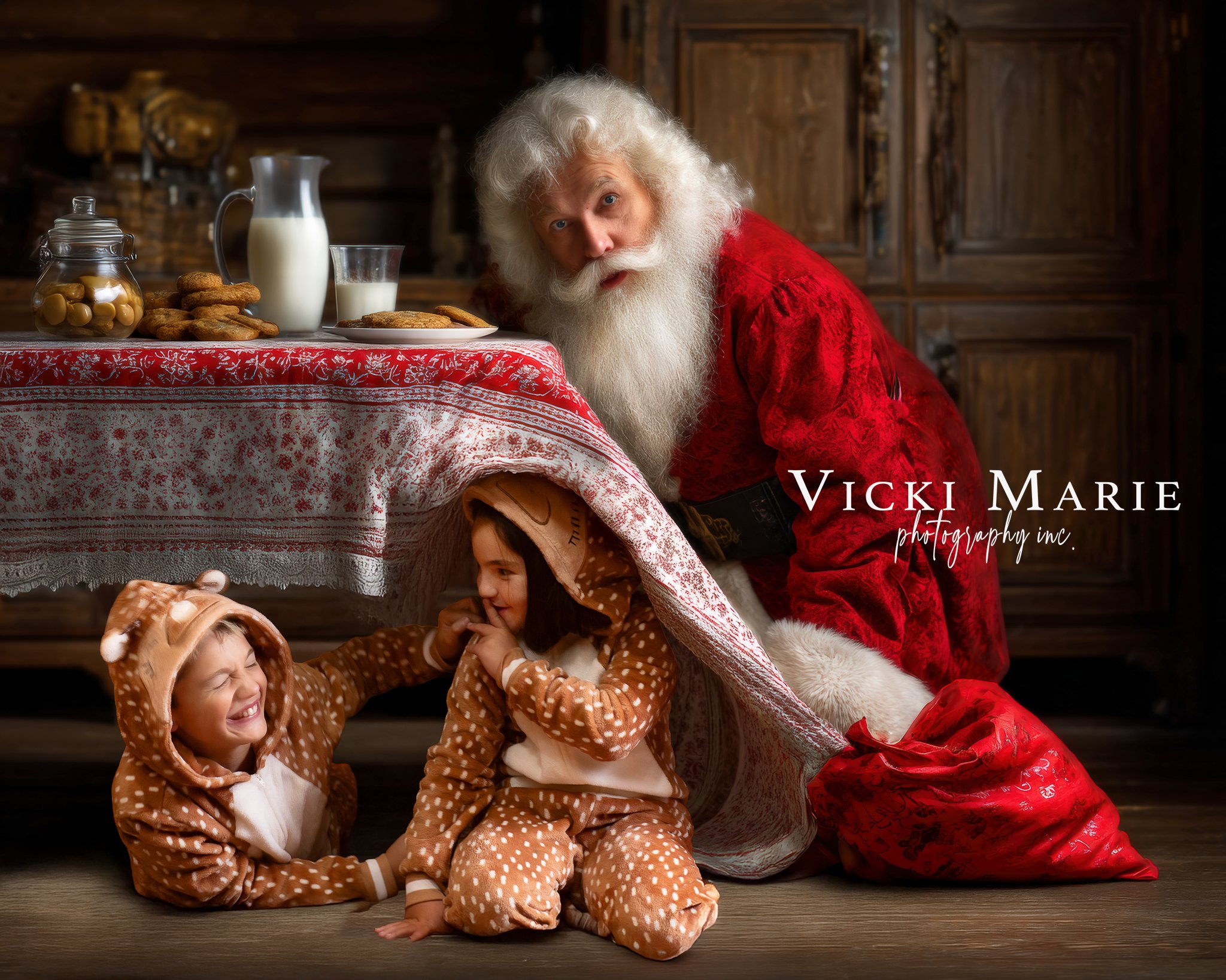 Santa Claus with children in reindeer pajamas under a tablecloth, in a cozy wooden room
