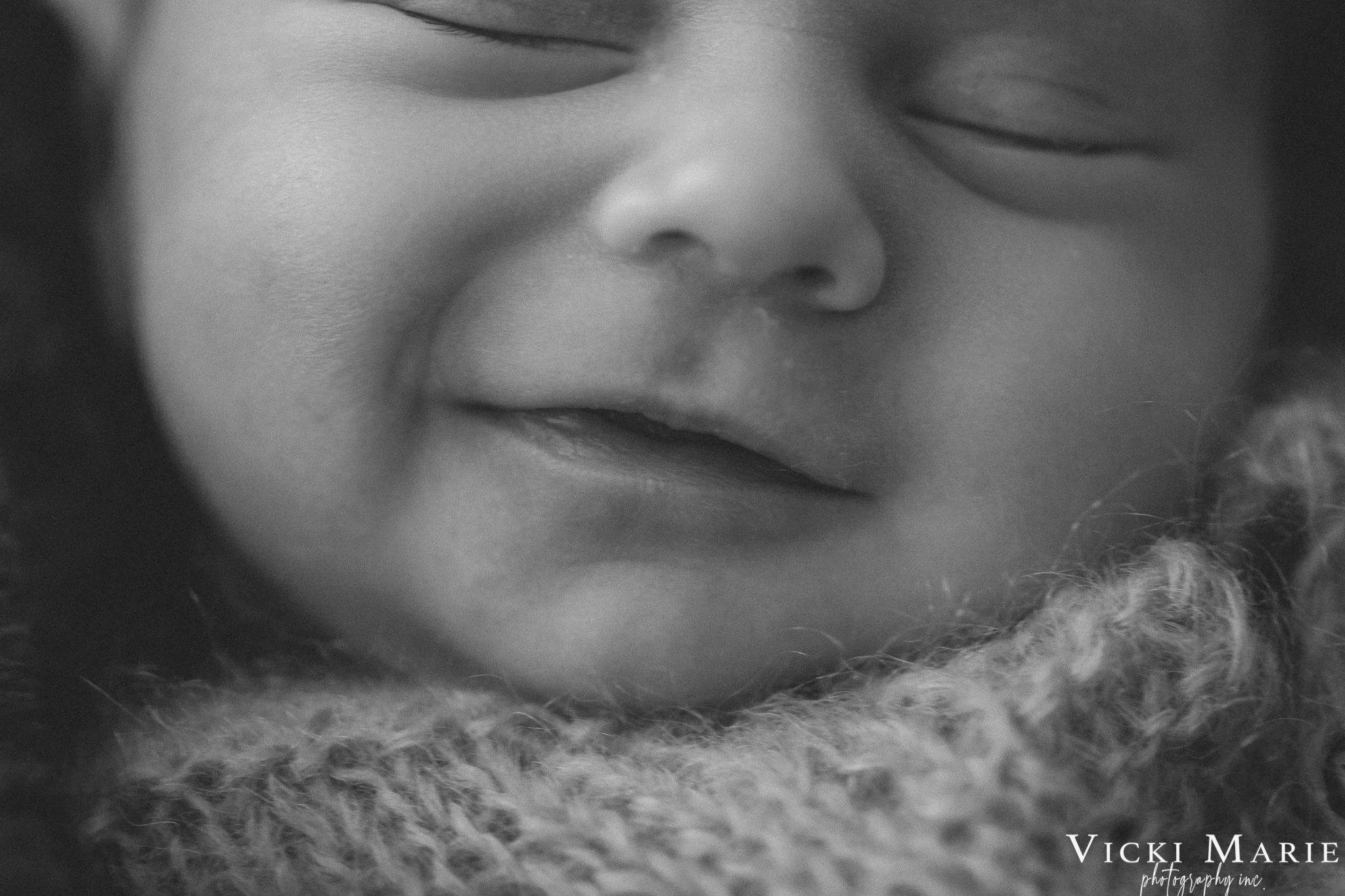 Close-up black and white photo of a smiling child's face with closed eyes, resting on a soft, textured surface.