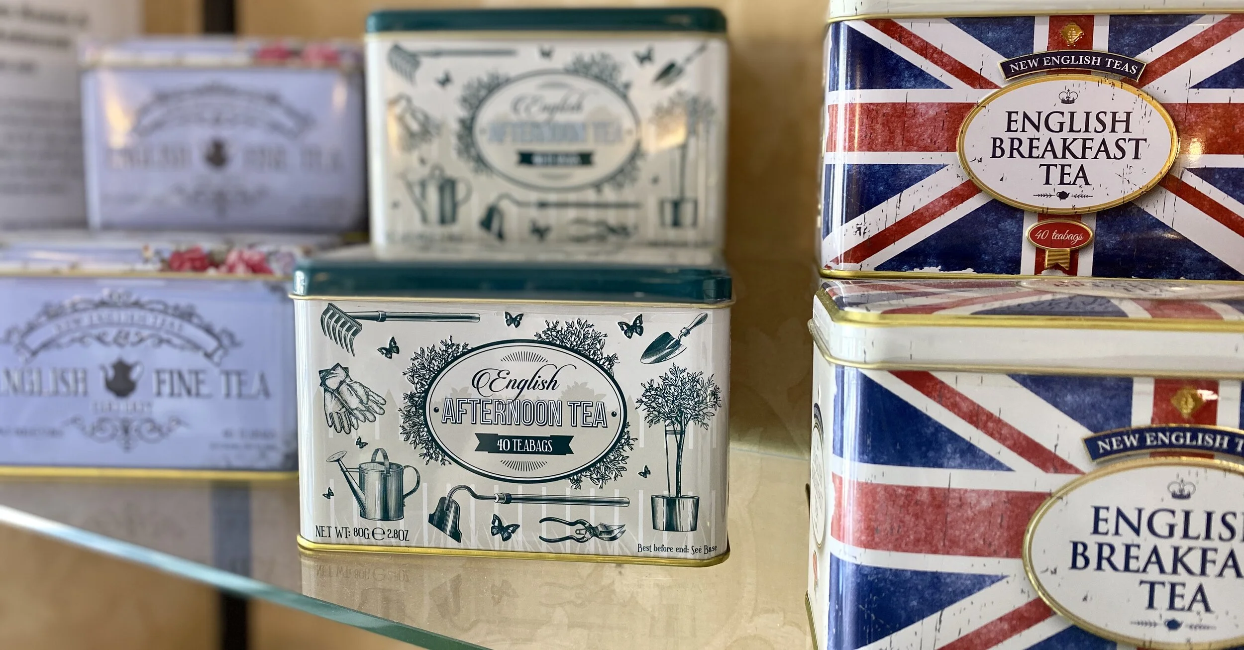 Assorted tins of tea, including English Breakfast Tea and Afternoon Tea, decorated with images and British flag motifs, on a shelf.