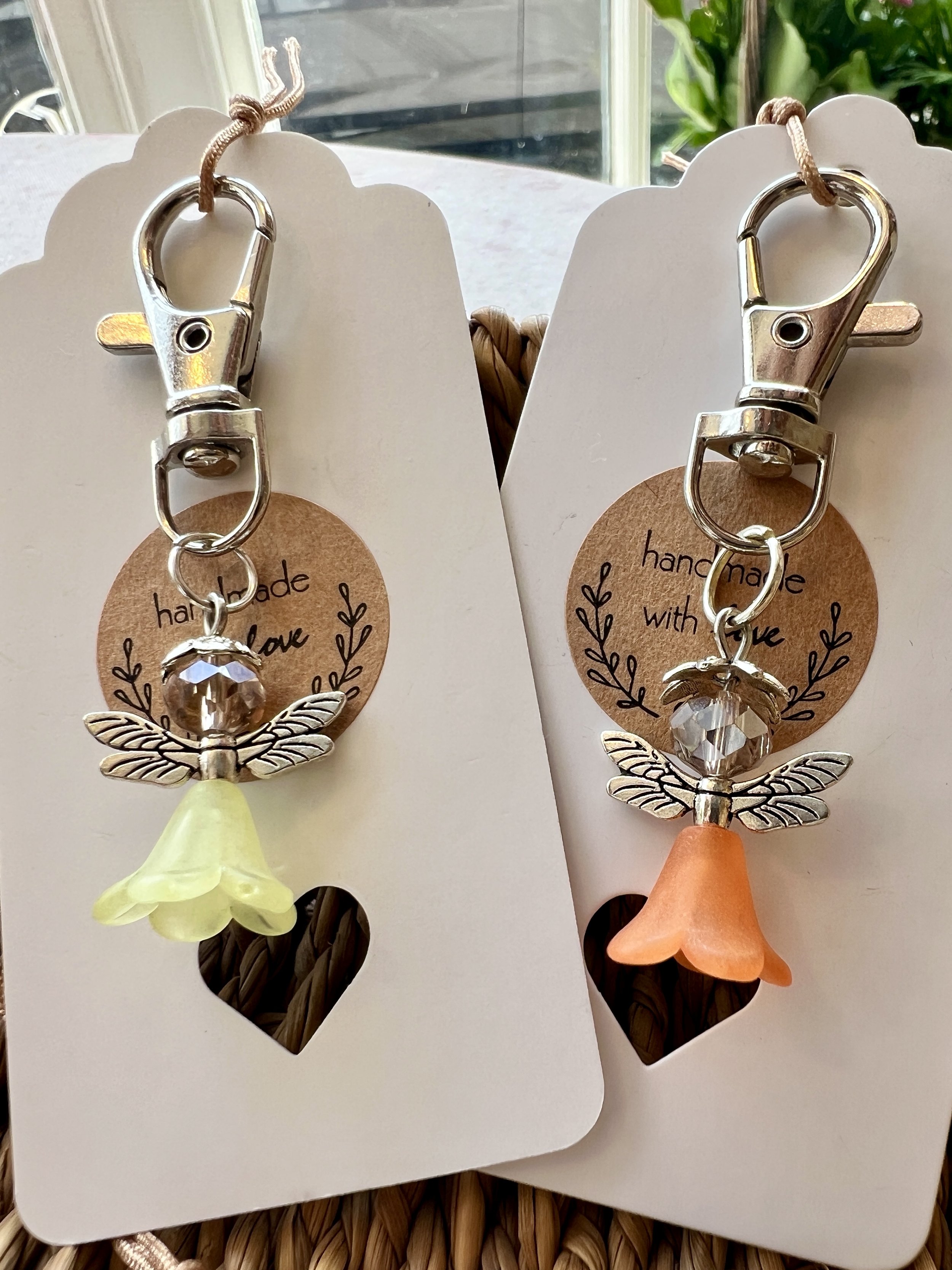 Close-up of two 'handmade with love' decorative keychains featuring a metallic dragonfly with crystal accents and small faux flower charms, attached to heart-shaped backing cards.