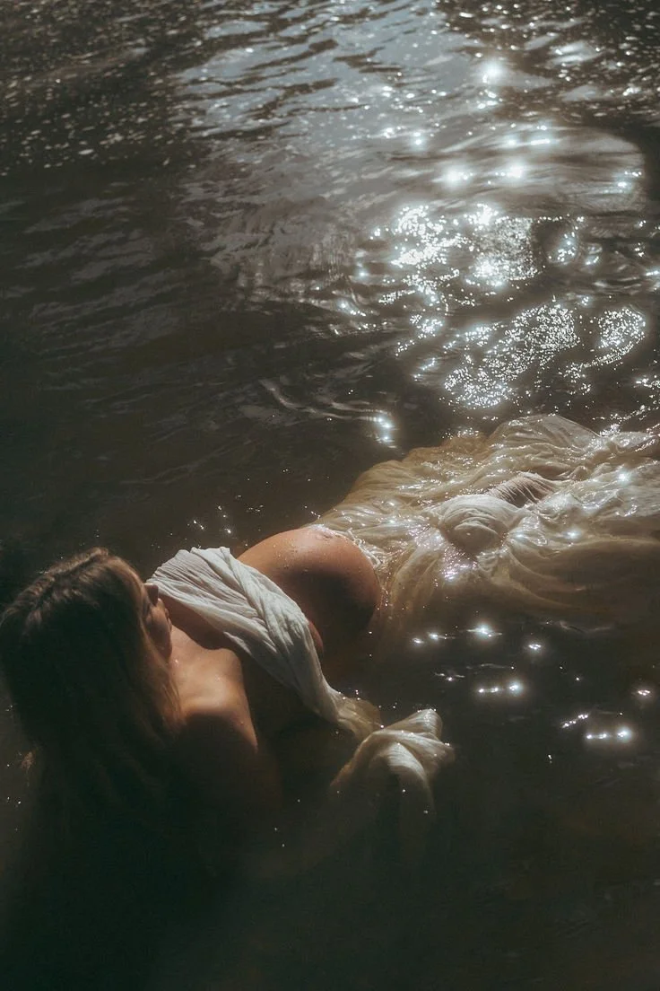 A person is lying on a body of water, partially submerged, with sunlight reflecting off the water's surface.
