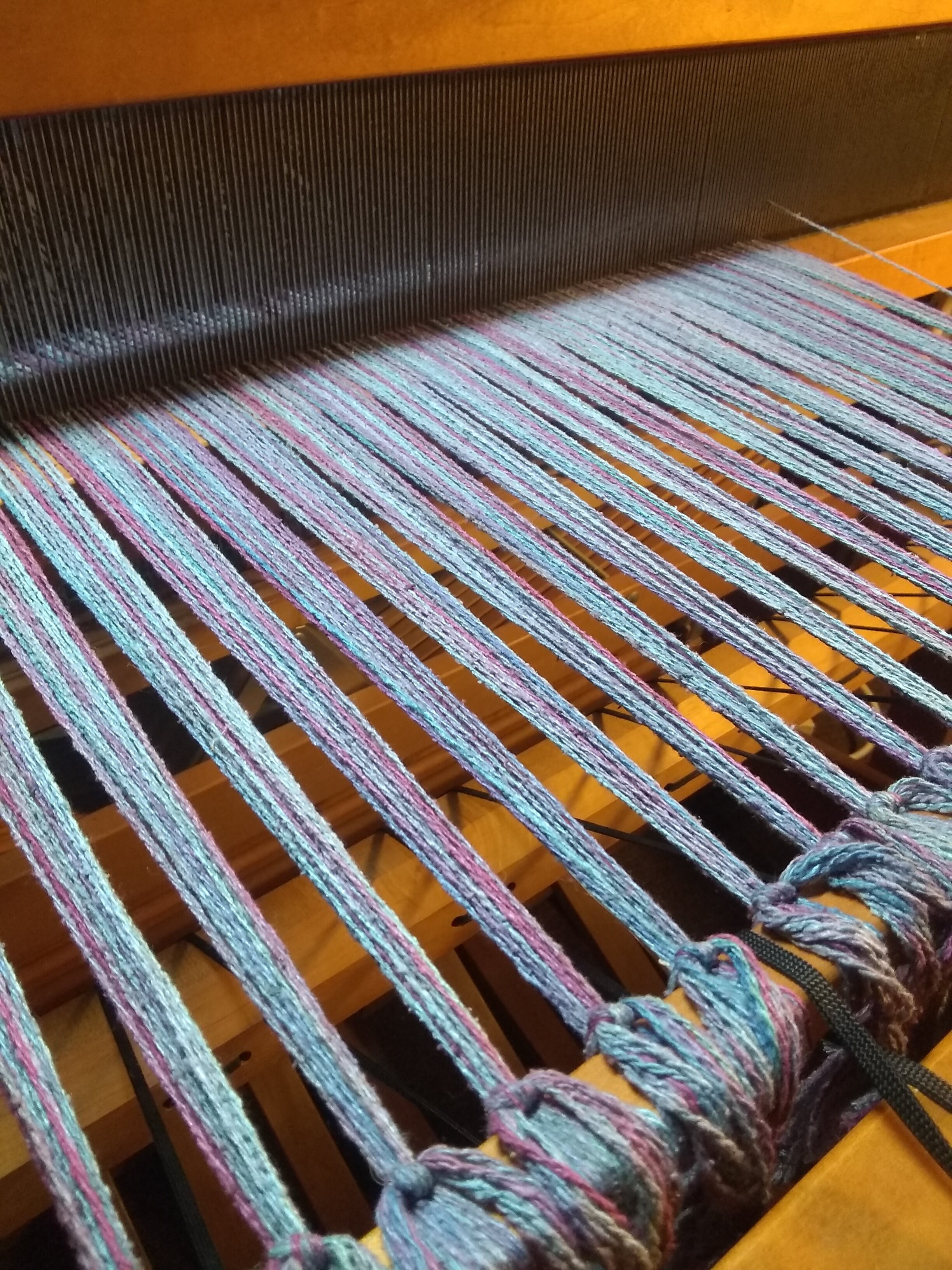 To maintain the correct spacing between warp yarns, each piece is threaded through the reed and then the heddles. The order of the threading through the heddles (not pictured) determines the woven pattern.