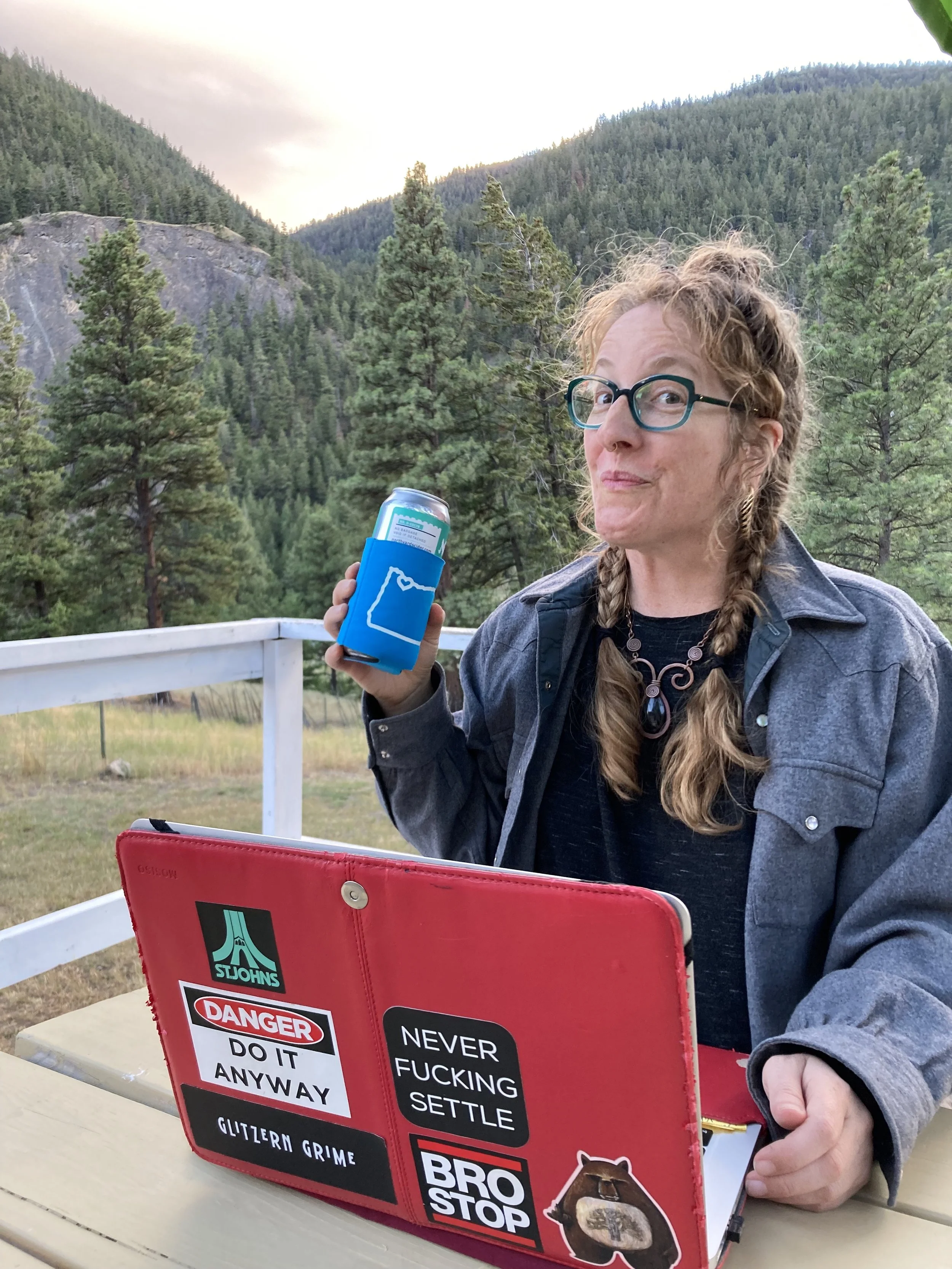 Color outdoor photo of Meghan smiling at the camera in front of her laptop with the mountains in the background.