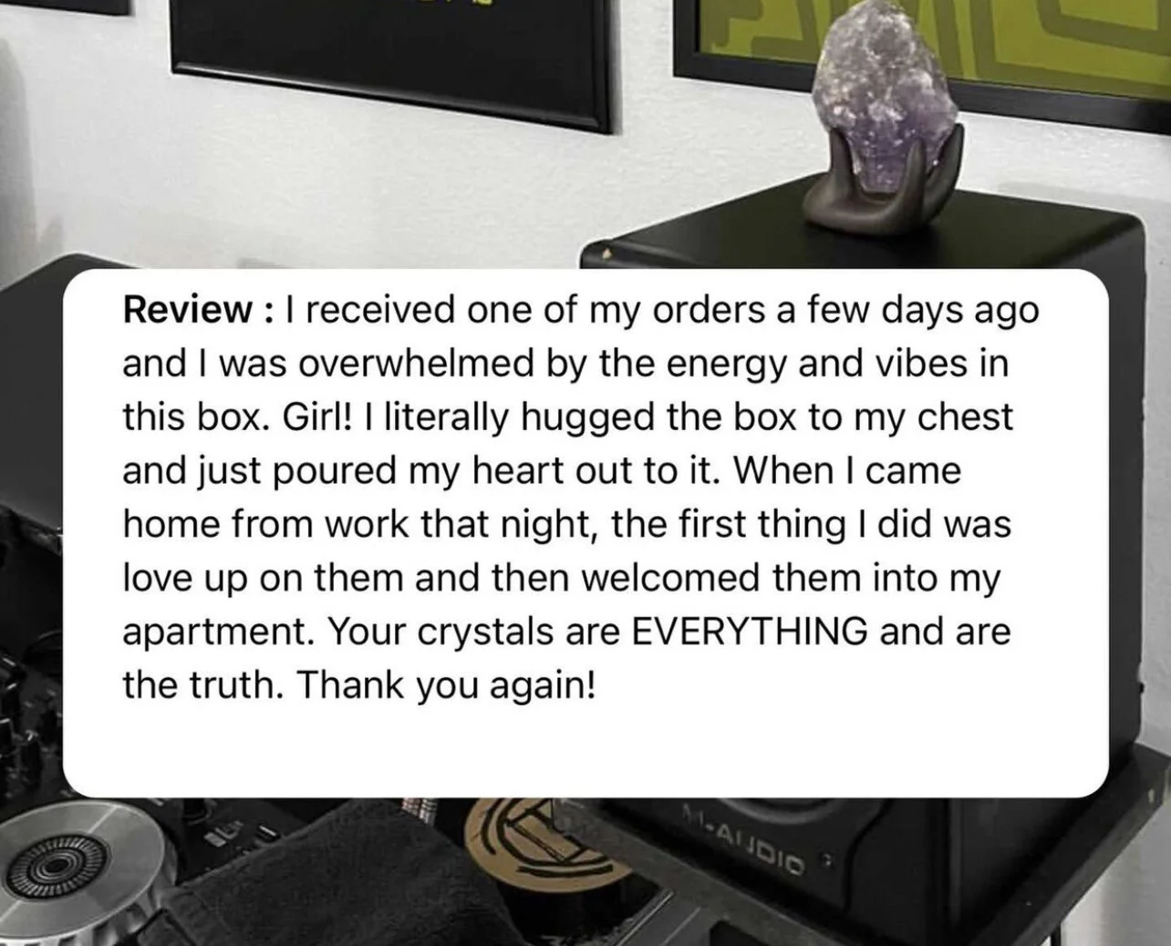 A review overlay on a photo of a black box with a purple crystal on top, placed on a black surface in a room with wall art.