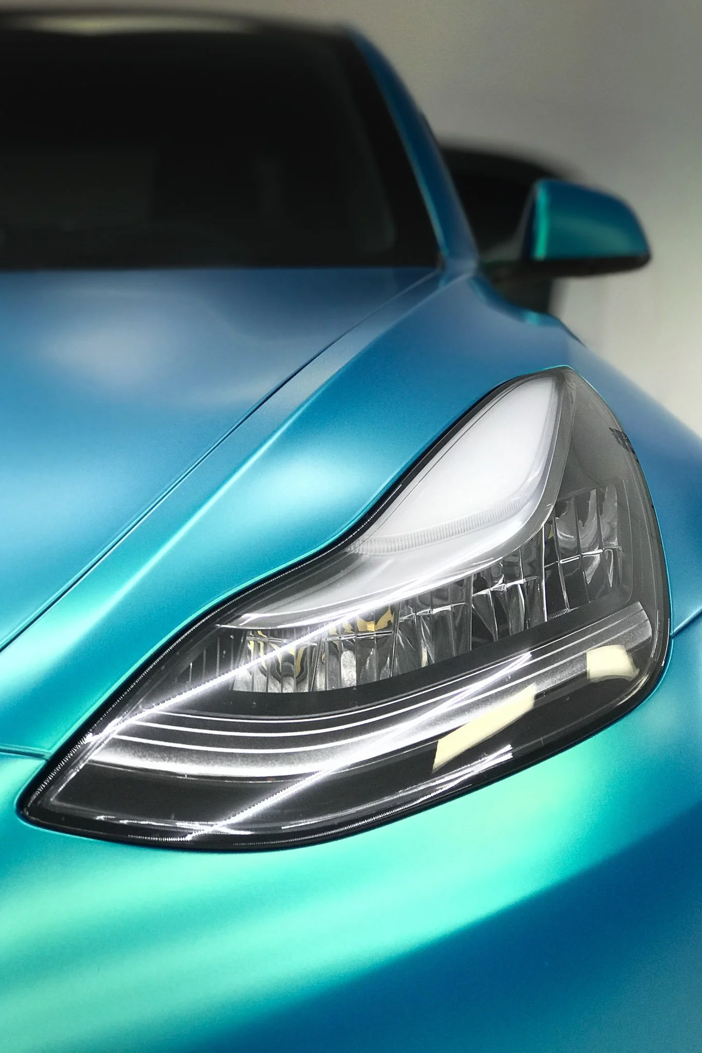 Close-up of a vehicle finished in a teal-to-blue color-shift vinyl wrap, showing the headlight and hood - EIGHTYNINE VWS custom vehicle wrap service in Little Elm, TX