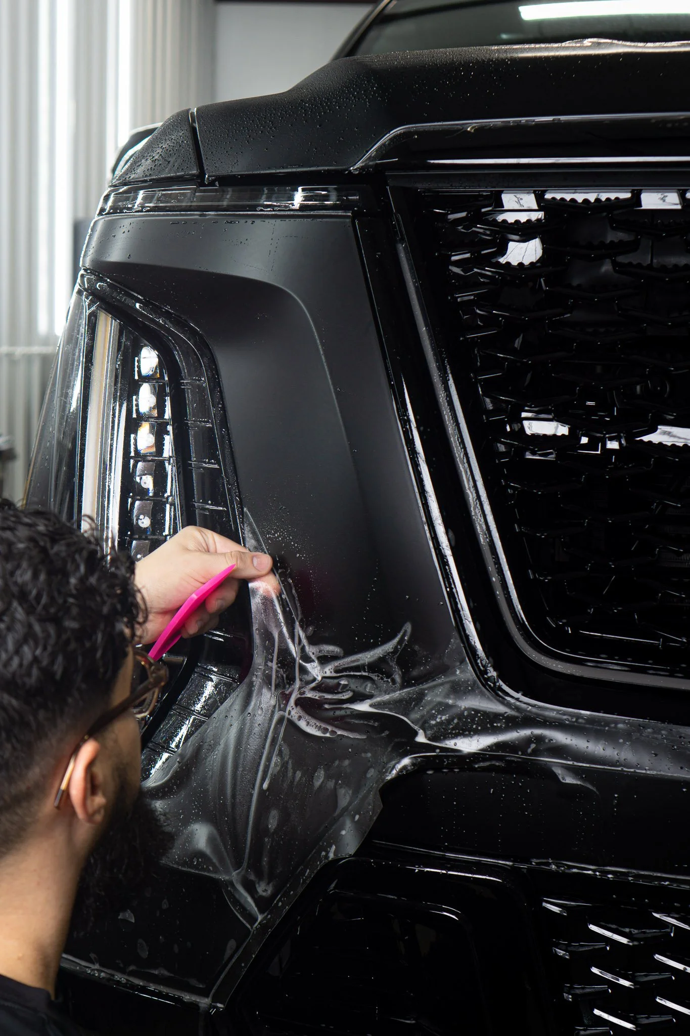 EIGHTYNINE VWS technician installing paint protection film on the front bumper and grille of a black Cadillac Escalade in Little Elm, TX