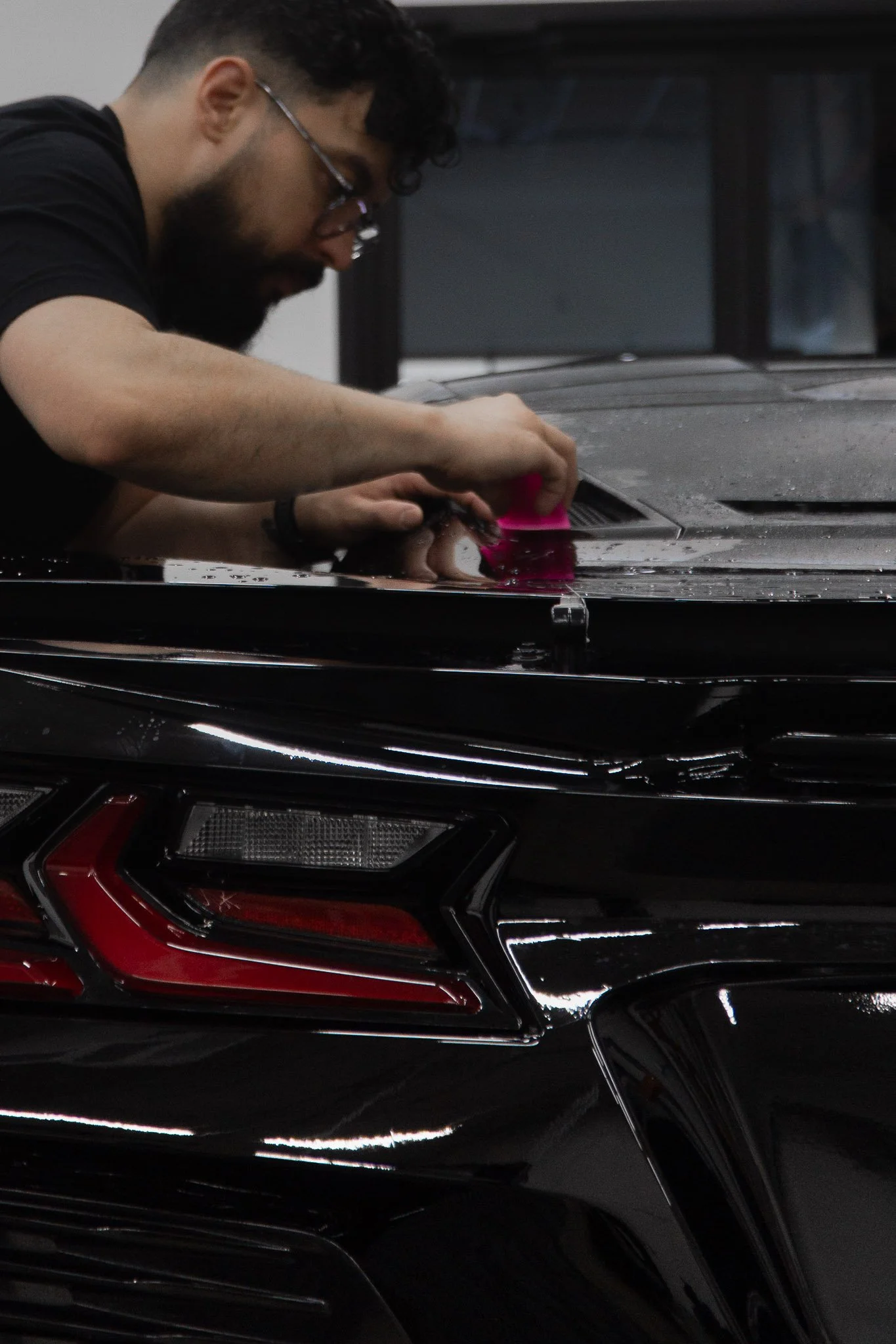 EIGHTYNINE VWS technician applying paint protection film near the taillight of a black sports car - professional PPF installation in Little Elm, TX