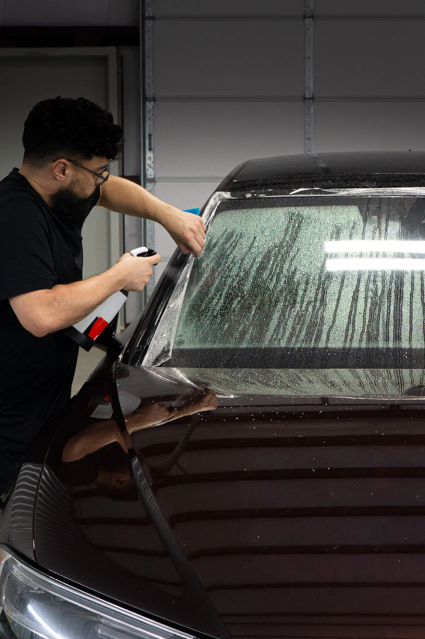 Technician spraying and squeegeeing automotive window film onto a vehicle windshield - EIGHTYNINE VWS professional window tint and windshield protection film installation in Little Elm, TX