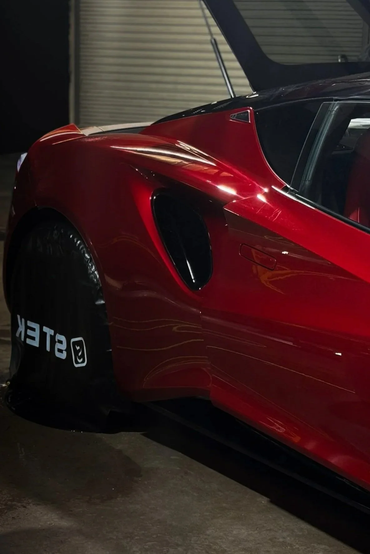 Red sports car parked beside a STEK-branded wheel cover after paint protection film installation - EIGHTYNINE VWS uses STEK PPF in Little Elm, TX