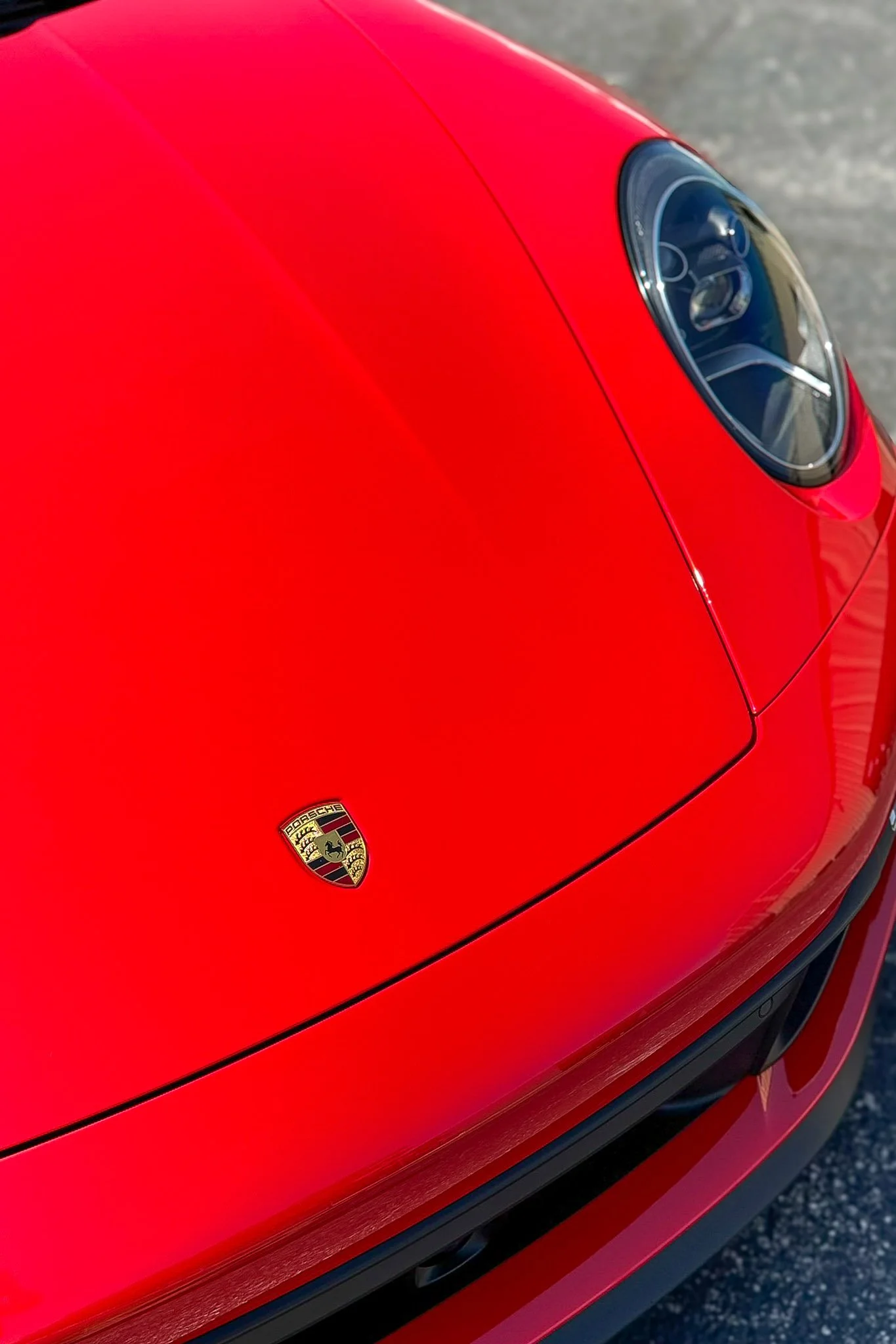 Close-up of the front hood and headlight of a red Porsche with clear paint protection film applied, Porsche crest visible - EIGHTYNINE VWS PPF service in Little Elm, TX
