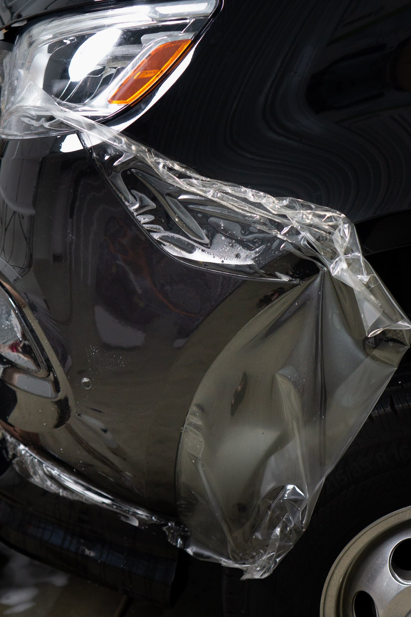 Close-up of paint protection film being applied to a black vehicle's headlight and fender during installation - EIGHTYNINE VWS PPF service in Little Elm, TX